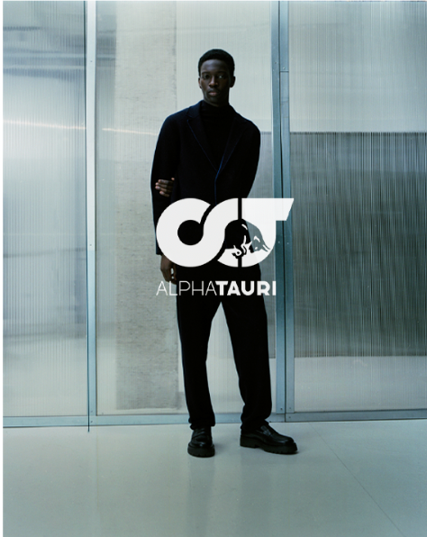 Mann in schwarzem Outfit steht vor moderner Kulisse mit AlphaTauri-Logo.