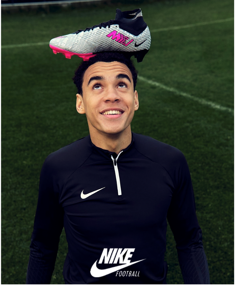 Junger Mann balanciert lächelnd einen Fußballschuh auf seinem Kopf auf einer Wiese. Er trägt ein Nike-Shirt.