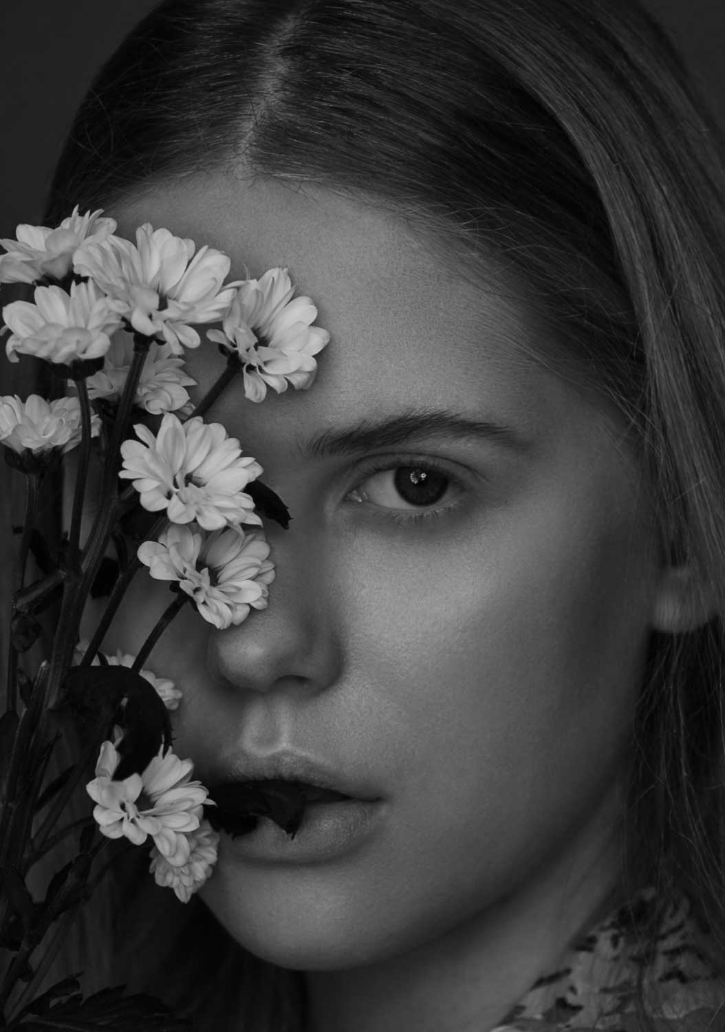 Schwarz-Weiß-Nahaufnahme einer jungen Frau, deren Augen und Mund von Blumen verdeckt werden.