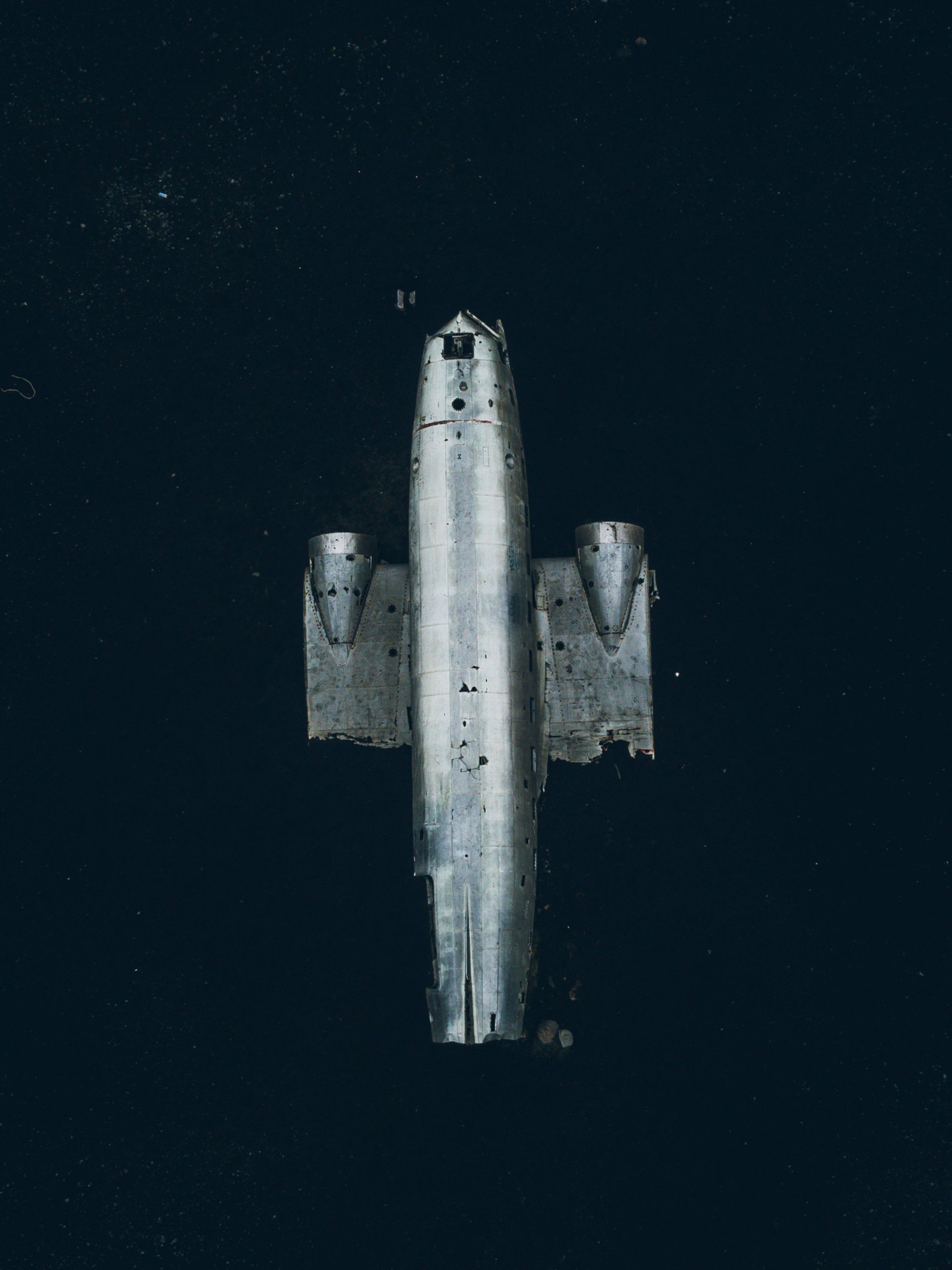 Luftaufnahme eines teilweise untergetauchten silbernen Flugzeugs in dunklem Wasser.