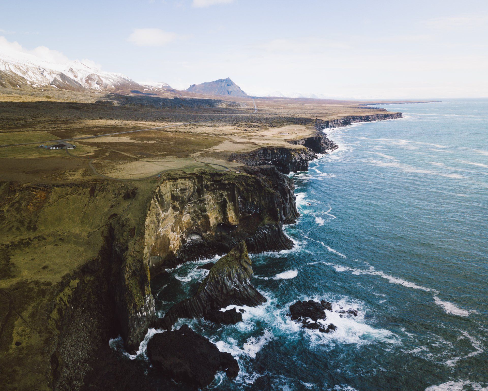 Zerklüftete Küste mit Klippen und tosenden Wellen, Berge im Hintergrund.