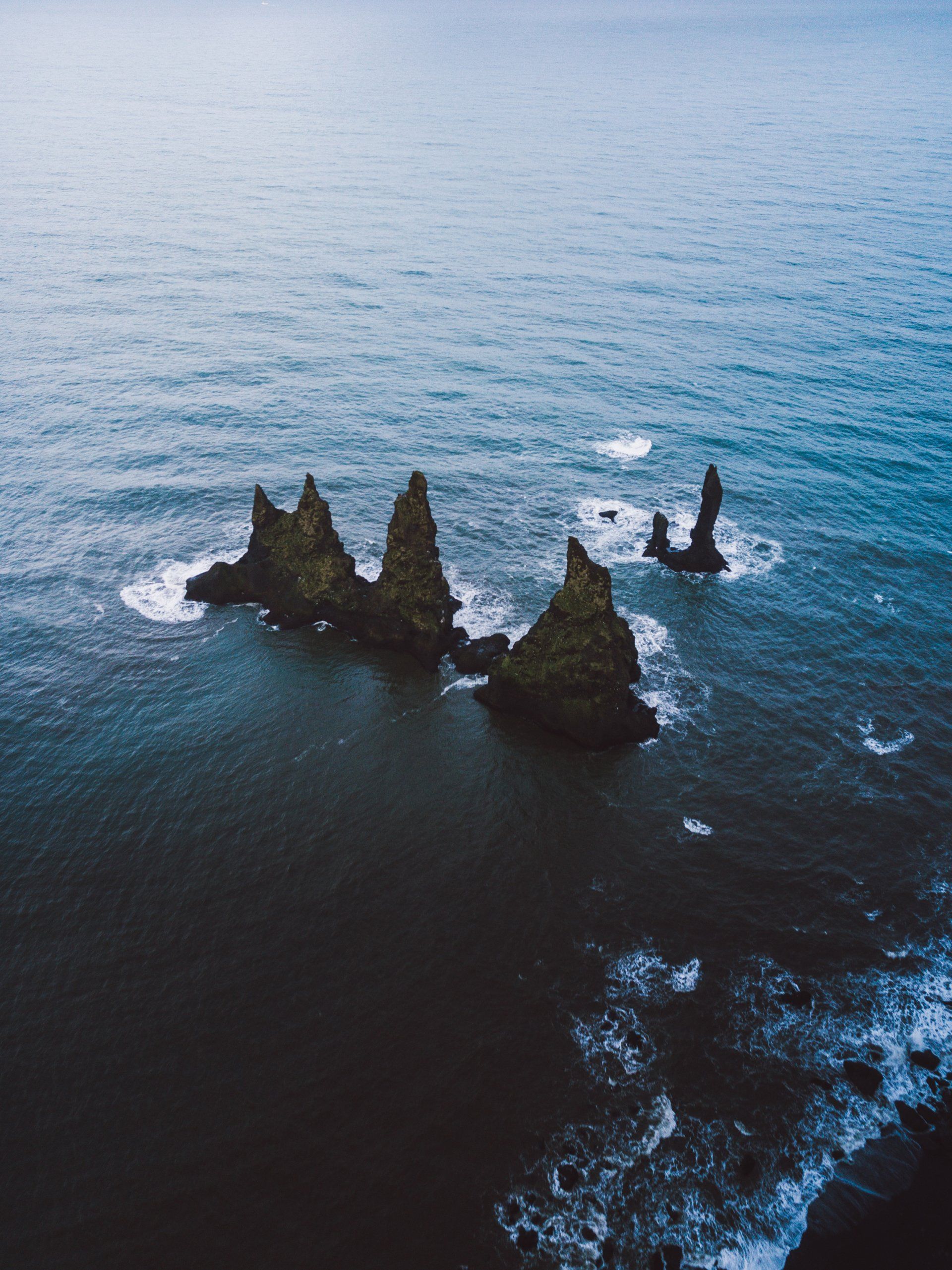 Dunkle, stimmungsvolle Meeresszene. Zerklüftete, dunkle Felsformationen ragen aus dem Meer; Wellen brechen um sie herum.