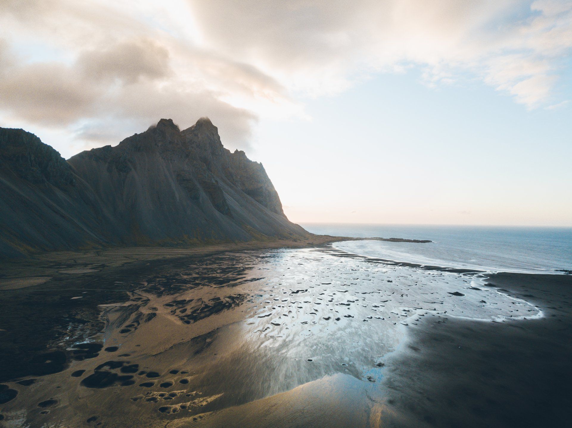 Bergkette neben einem schwarzen Sandstrand unter einem bewölkten Himmel.