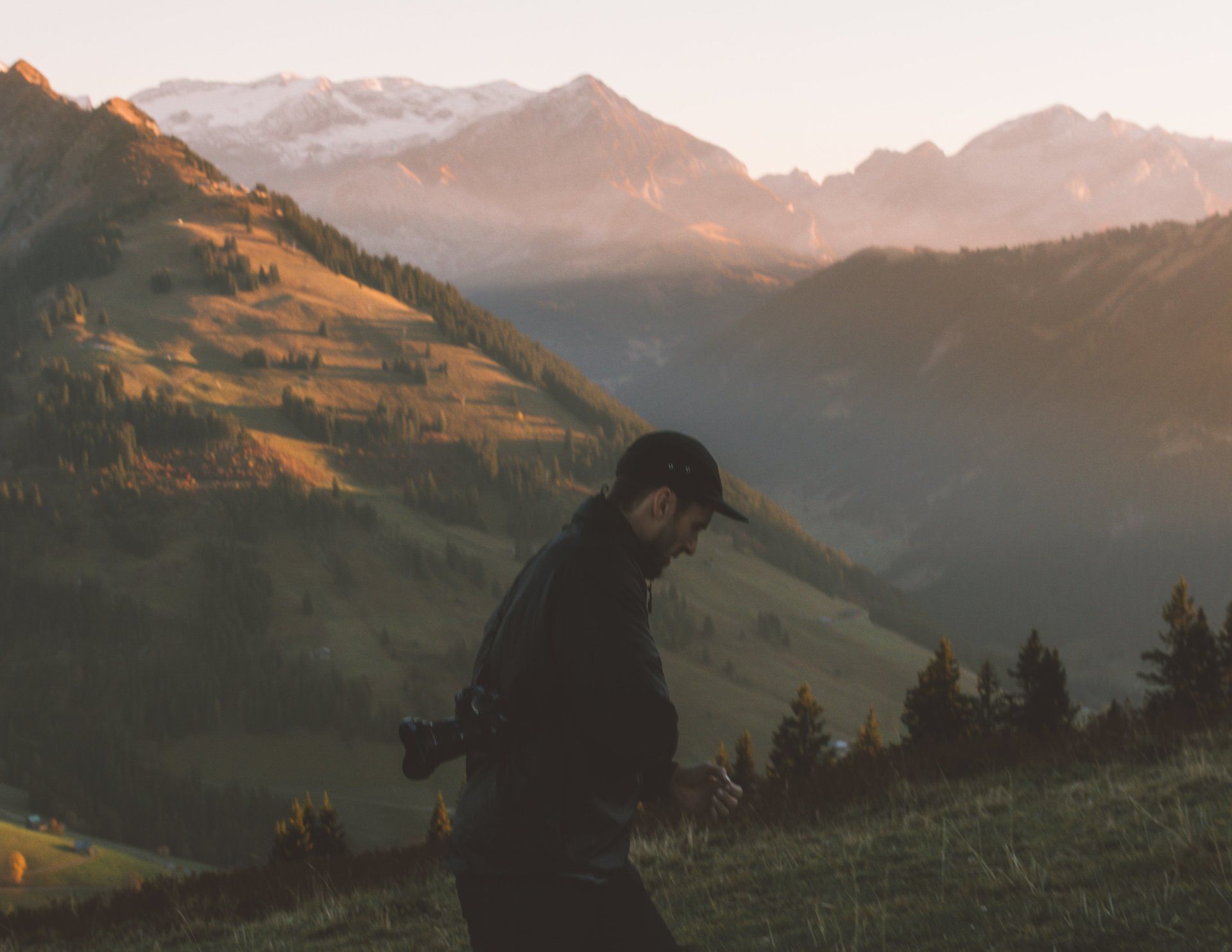 Mann geht auf einem grasbewachsenen Hügel mit Bergen im Hintergrund, in warmes Sonnenlicht getaucht.