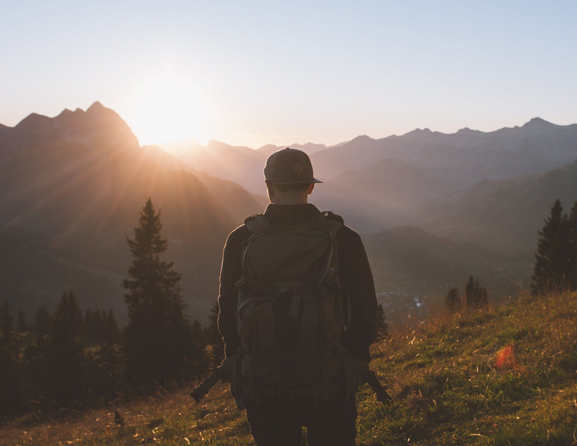 Wanderer mit Rucksack vor einem Sonnenaufgang über den Bergen. Goldenes Licht taucht die Landschaft in goldenes Licht.