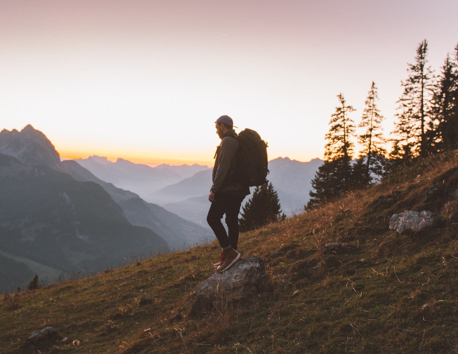 Wanderer auf einem Bergkamm, der bei Sonnenuntergang auf ein nebliges Tal blickt.