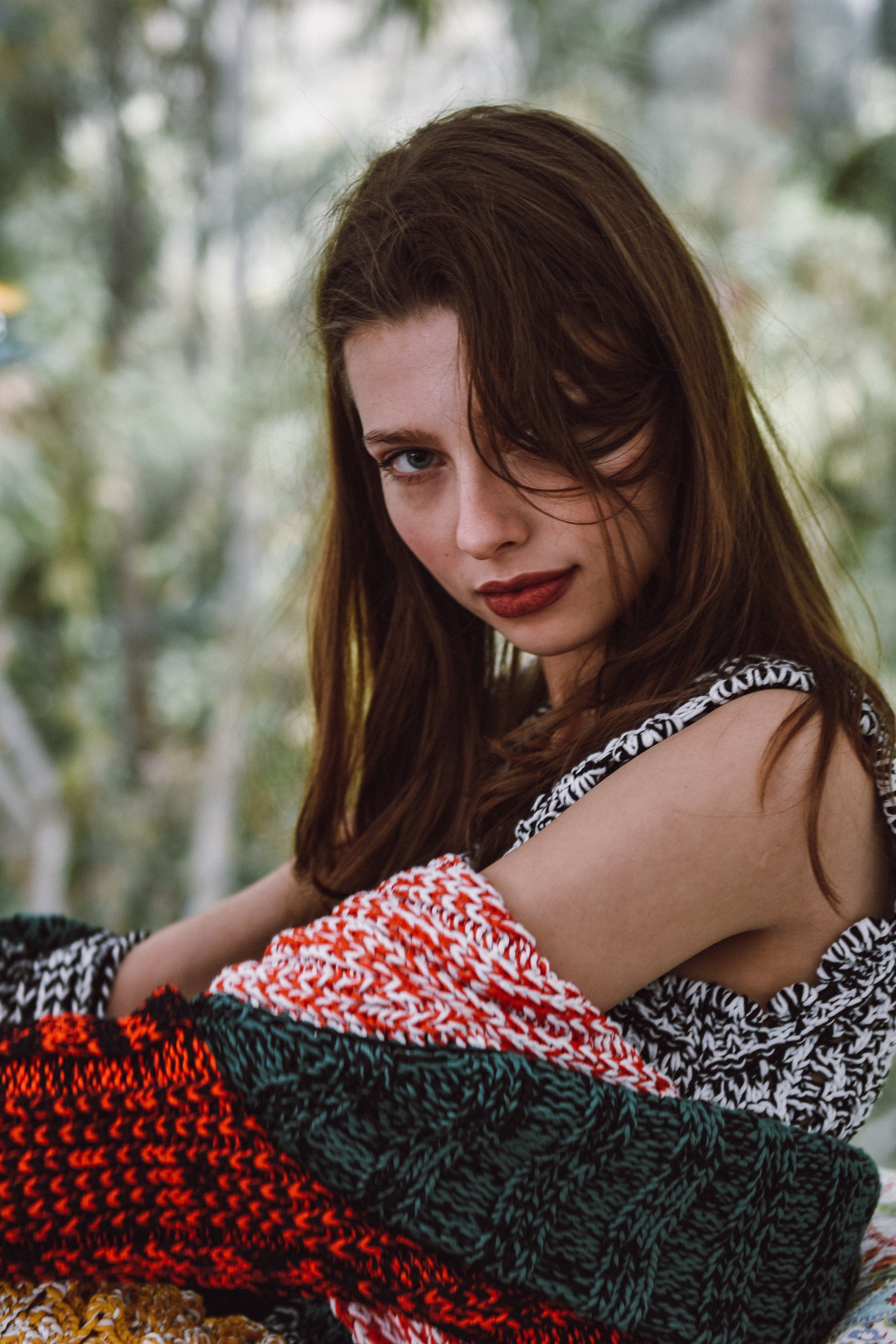 Eine in bunte Decken gehüllte Frau blickt den Betrachter im Freien an.