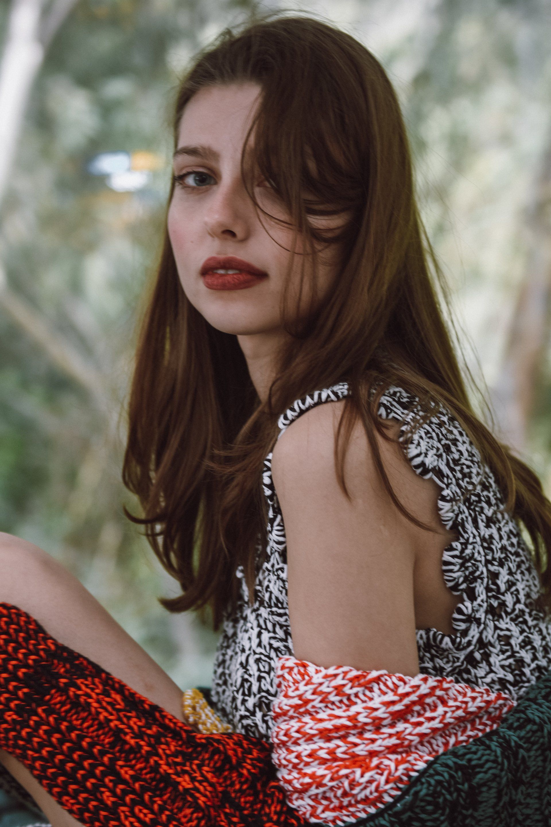 Frau mit braunem Haar, gemustertem Oberteil und rotem Lippenstift, blickt in die Kamera.