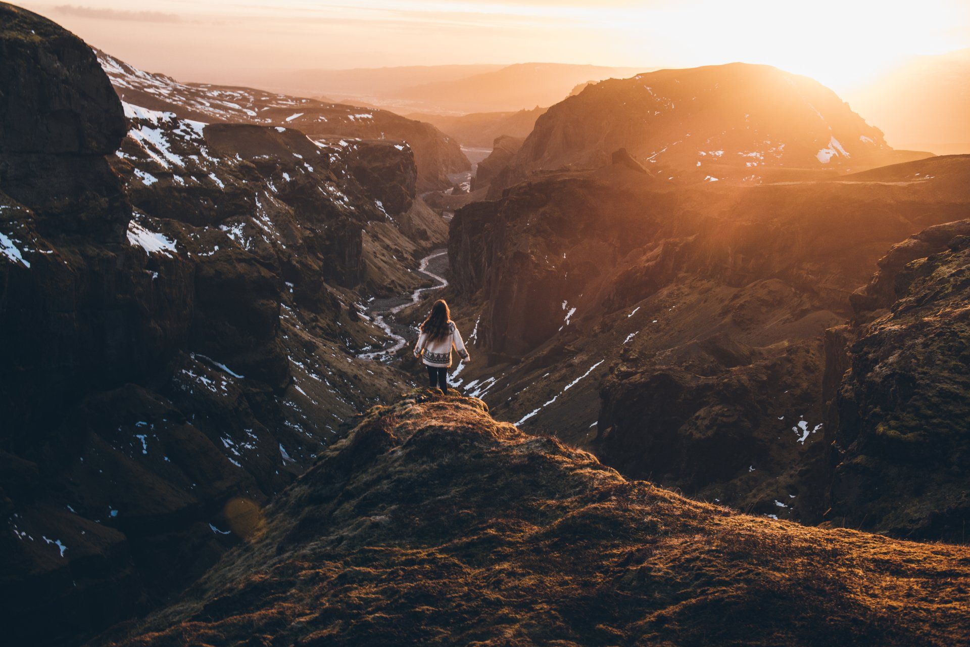 Frau steht auf einer Klippe und blickt bei Sonnenuntergang über eine Schlucht; warmes, goldenes Licht.