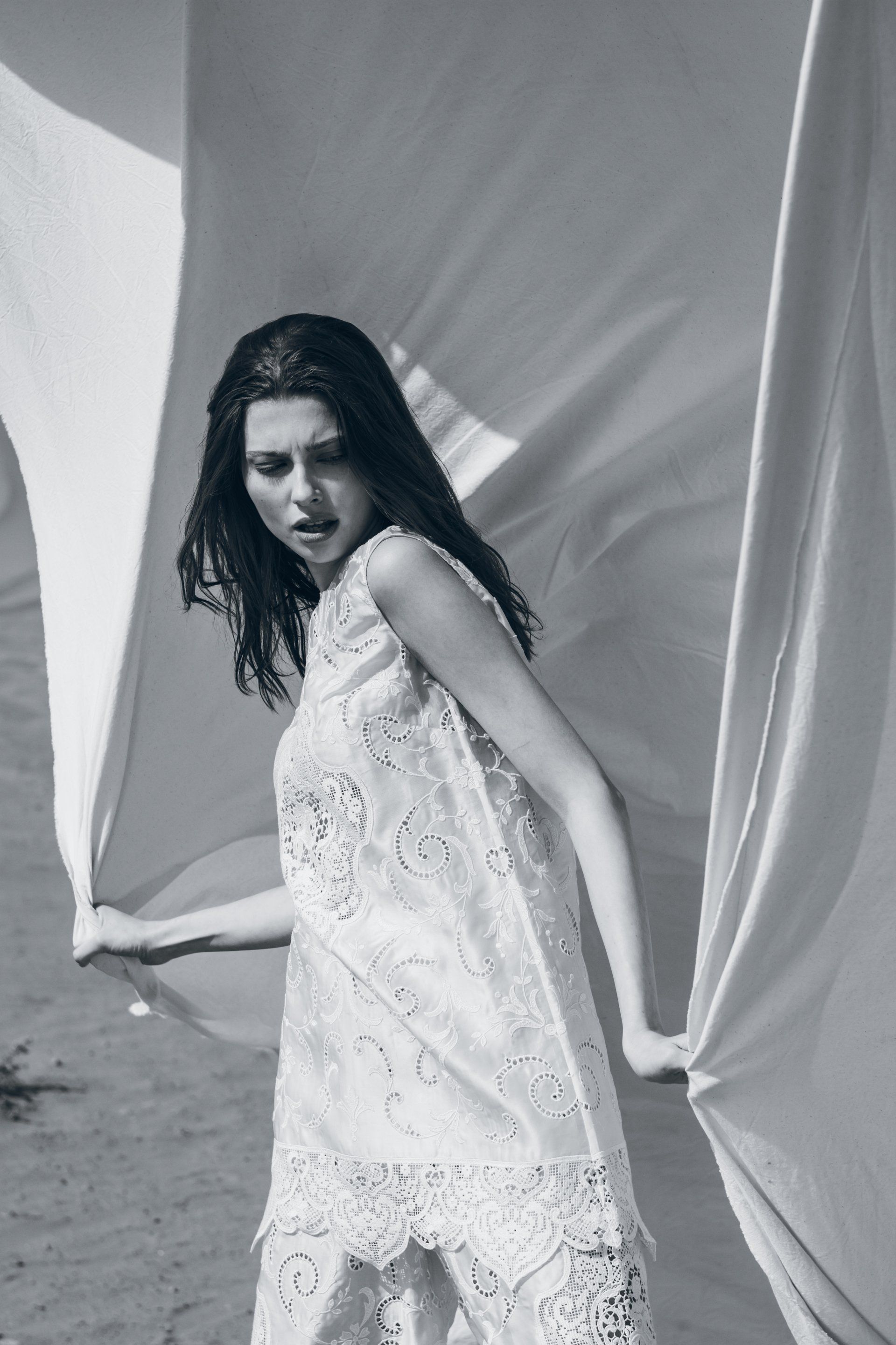 Frau im weißen Spitzenkleid hält Stoff, im Freien, erschrockener Gesichtsausdruck.