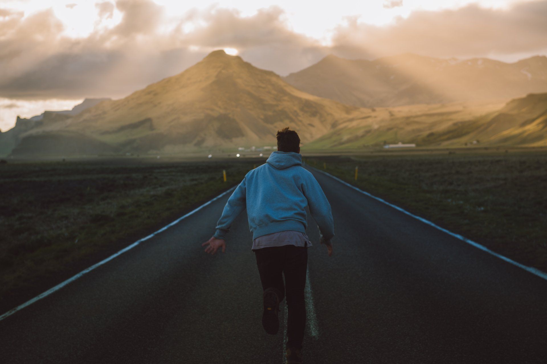 Person, die unter einem dramatischen Himmel auf einer Straße in Richtung Berge geht.