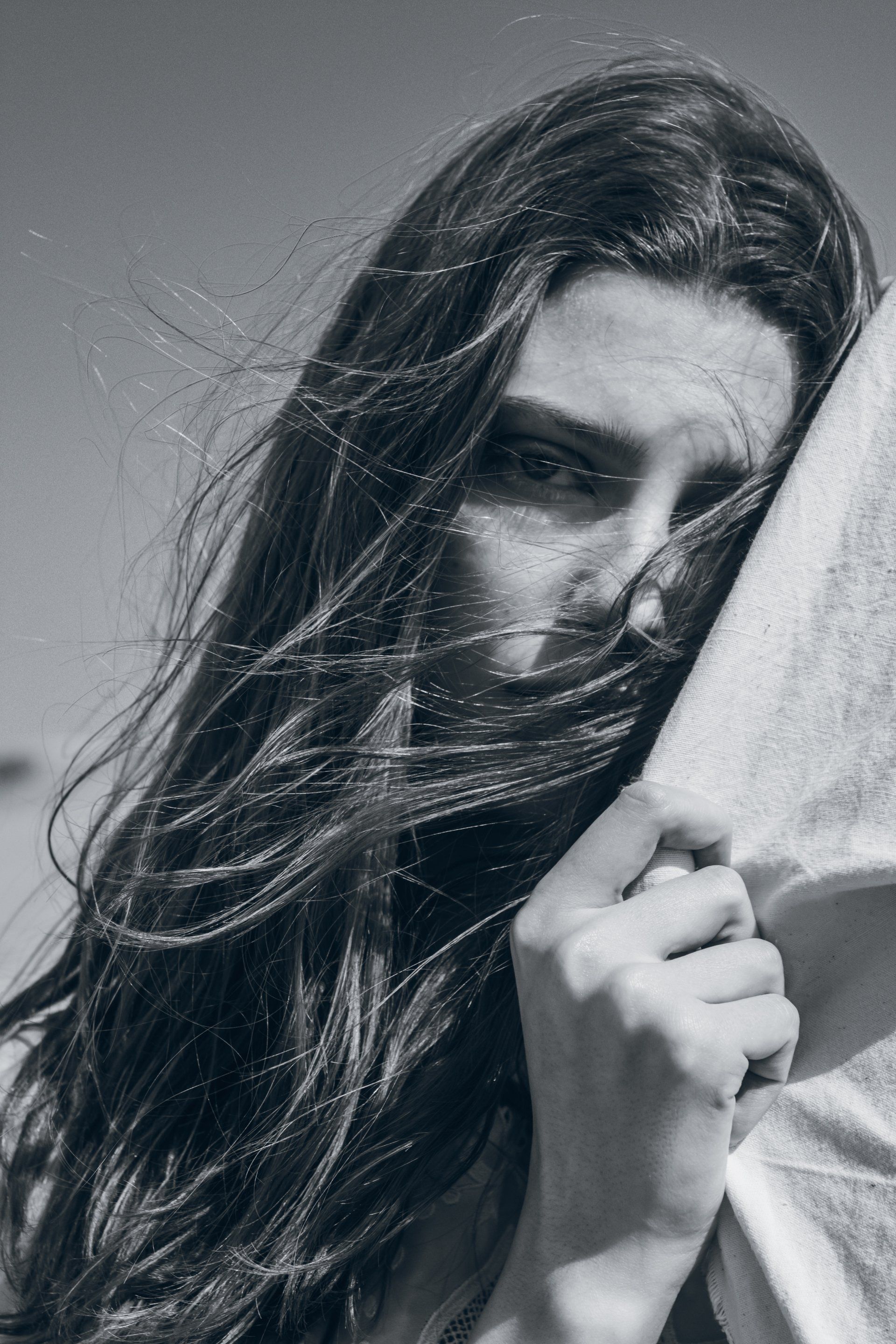 Frau mit vom Wind zerzaustem Haar, hält ein Handtuch und blickt in die Kamera.