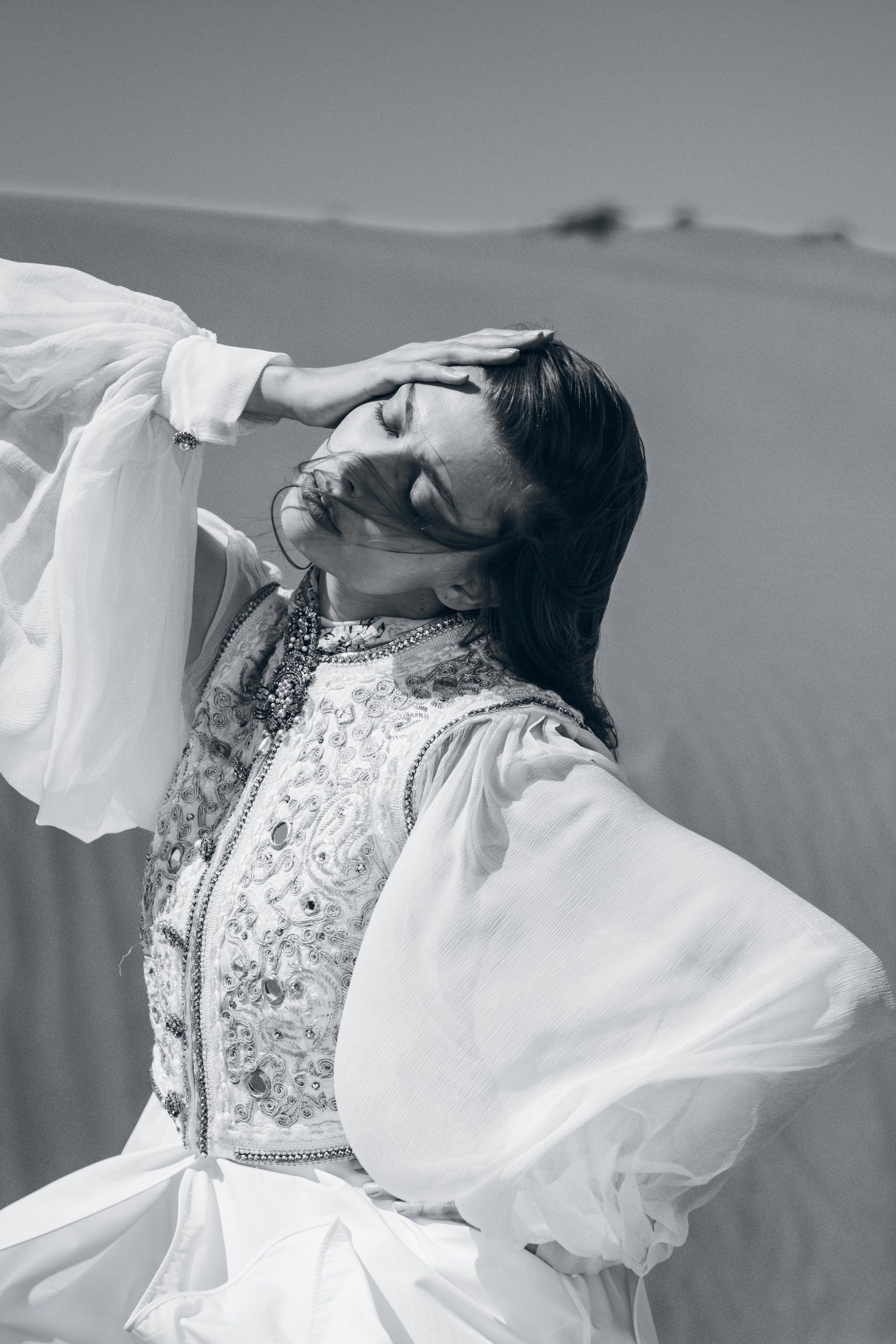 Frau im weißen Kleid in der Wüste, schützt ihre Augen vor der Sonne.