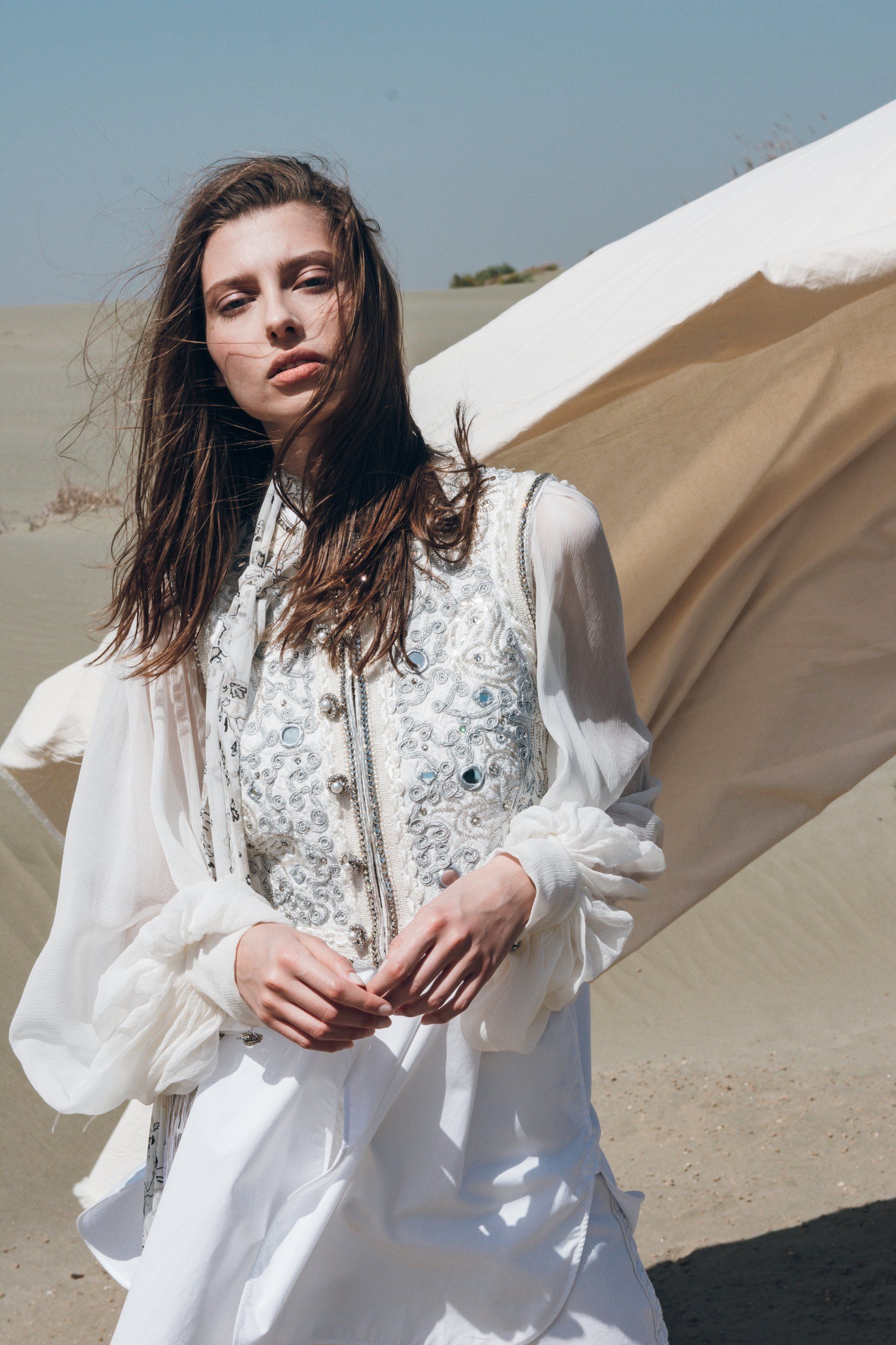 Frau in weißem Outfit mit Weste, wehender Stoff in der Wüste.