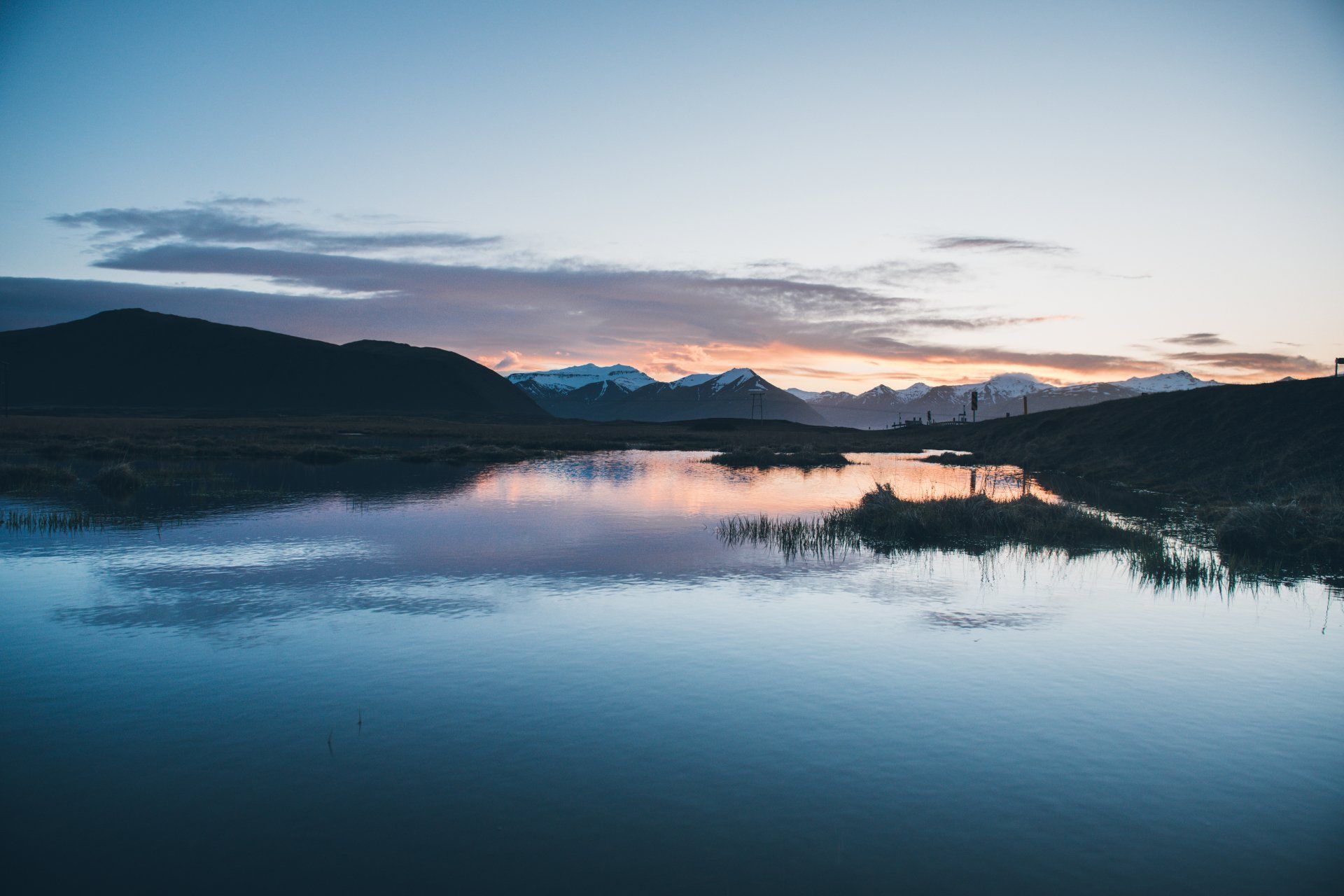 Berge spiegeln sich in der Abenddämmerung im ruhigen Wasser; blauer und orangefarbener Himmel.