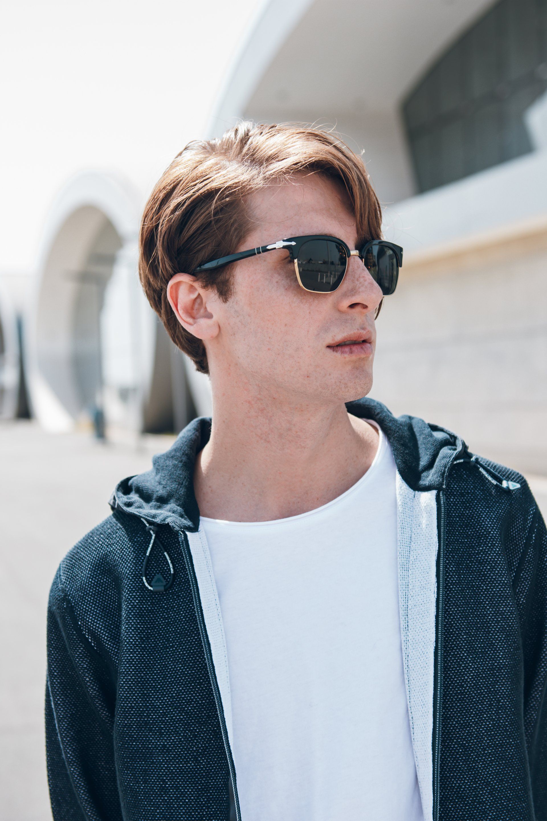 Mann mit Sonnenbrille und Kapuzenpullover schaut zur Seite ins Freie.