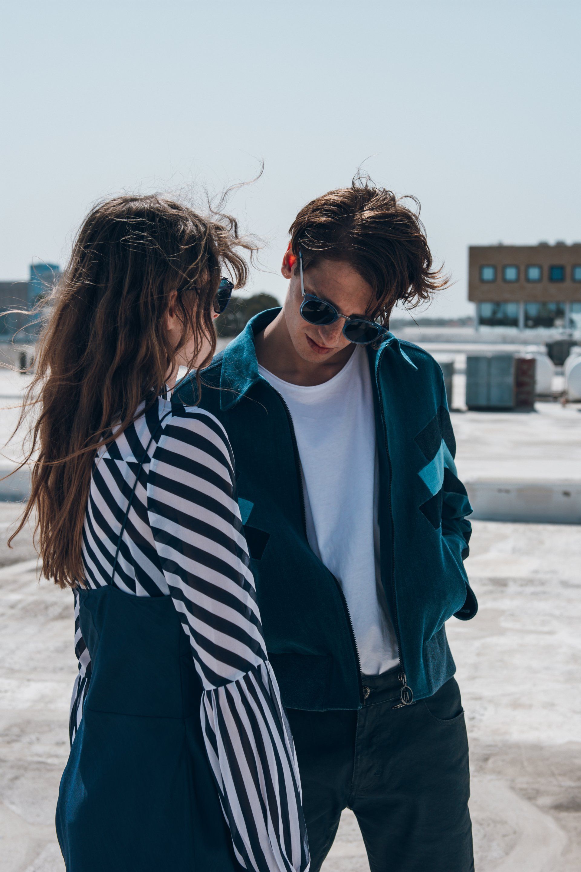 Ein Mann und eine Frau mit Sonnenbrillen auf einem Dach, der Mann schaut nach unten.