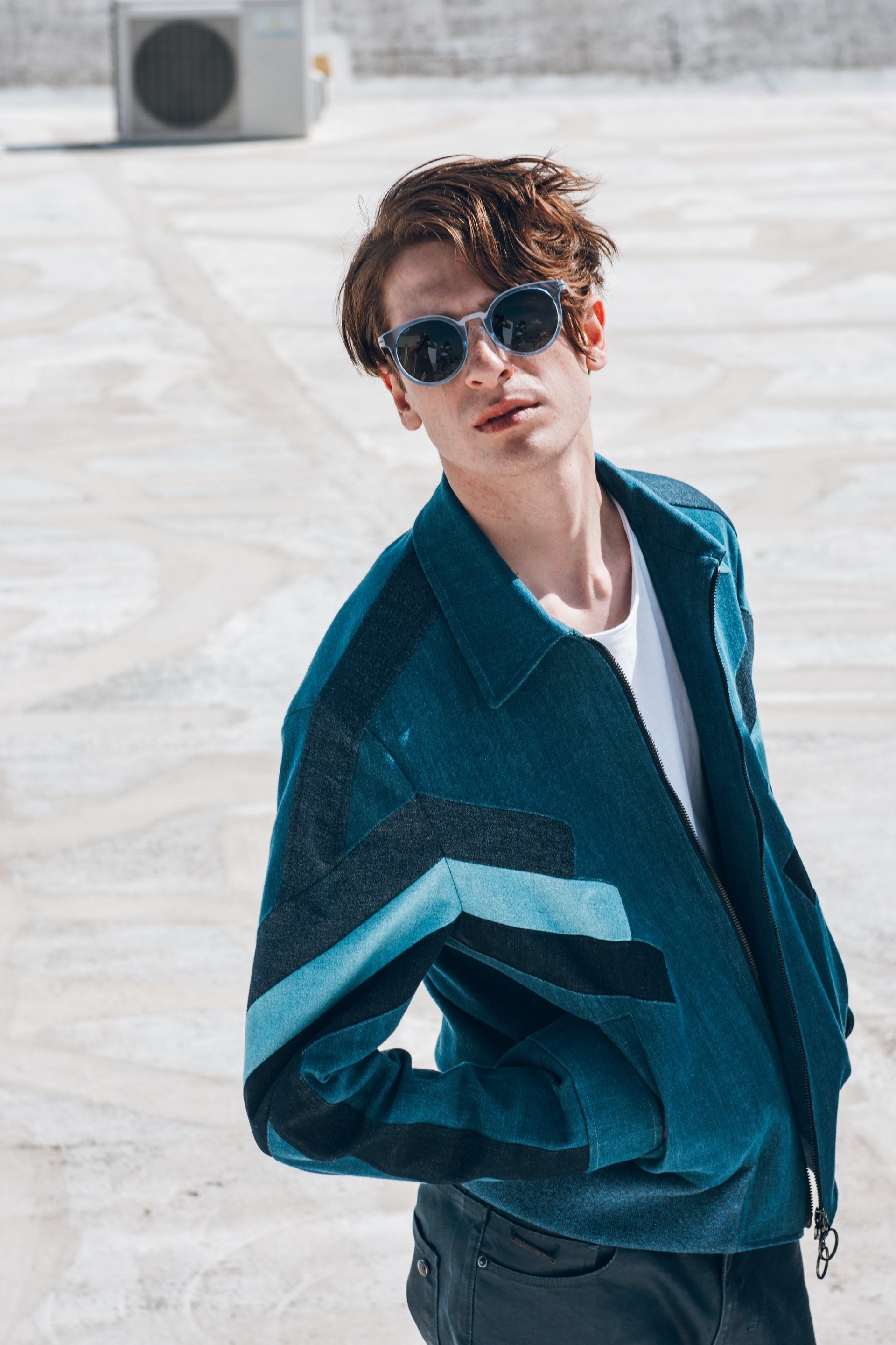 Mann mit Sonnenbrille, blauer Jacke und weißem Hemd auf einem Dach.