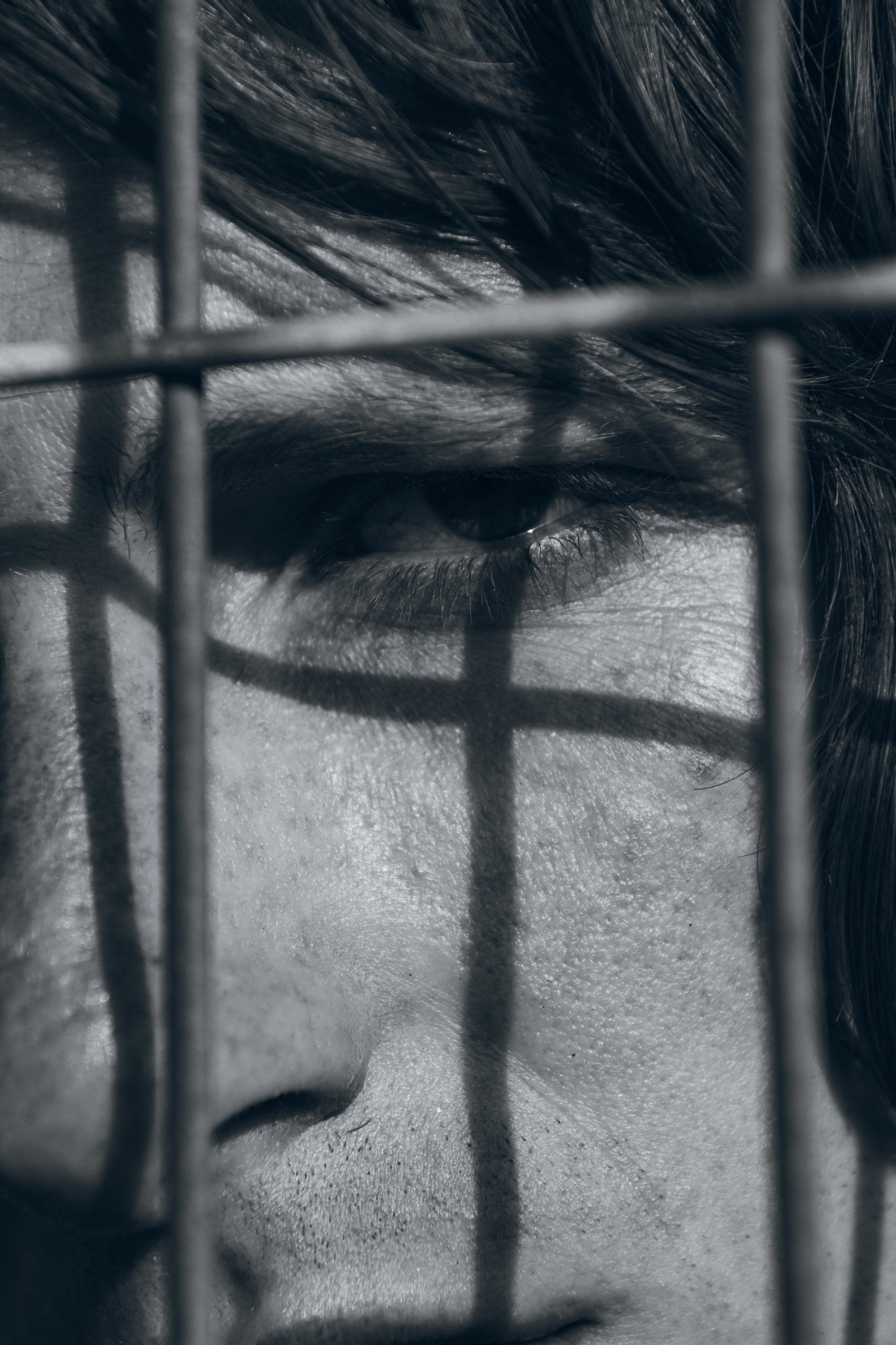 Nahaufnahme des Gesichts einer Person in Schwarzweiß mit Schatten eines Maschendrahtzauns.