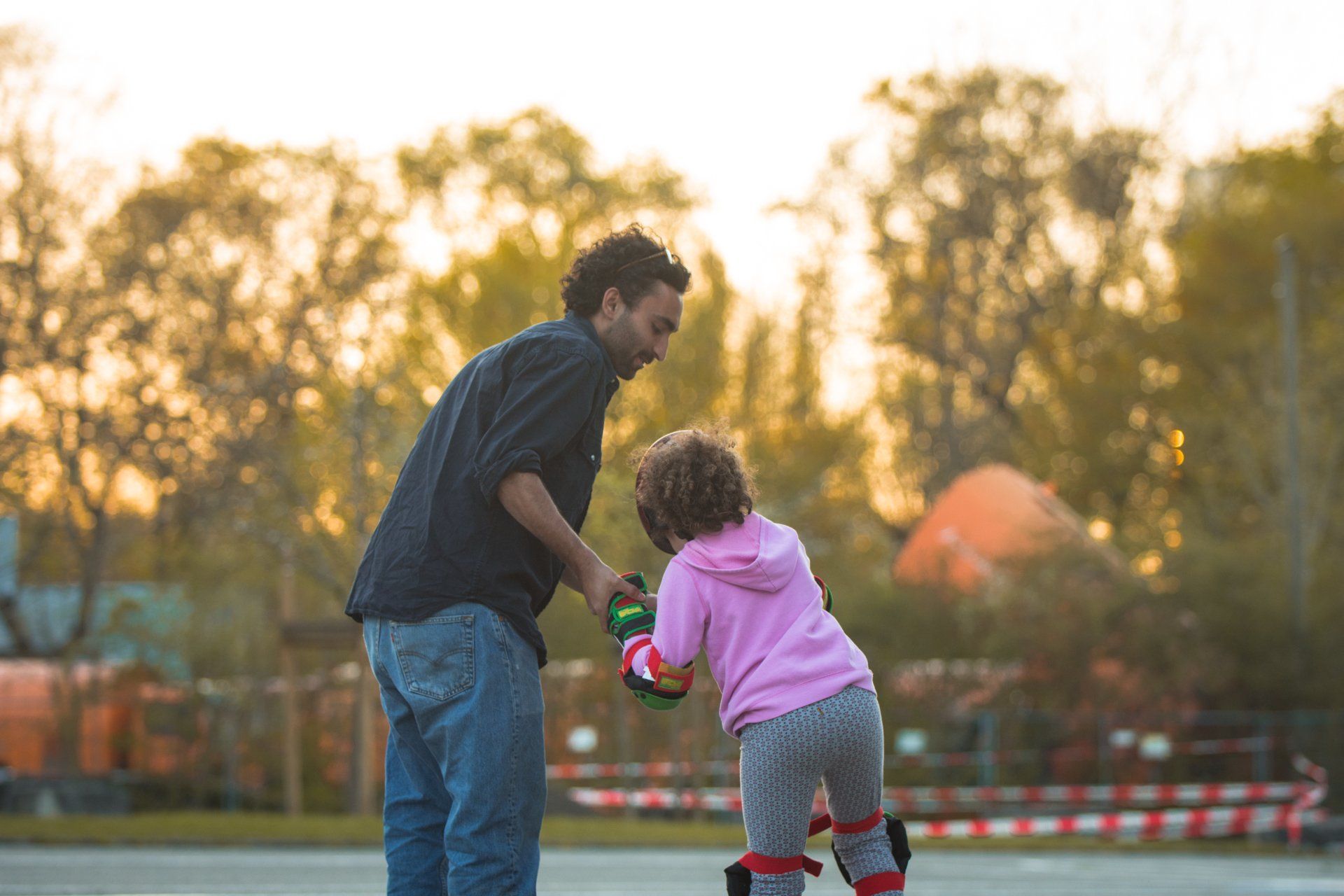 Mann hilft einem kleinen Kind bei Sonnenuntergang im Freien beim Anziehen der Rollschuhe.