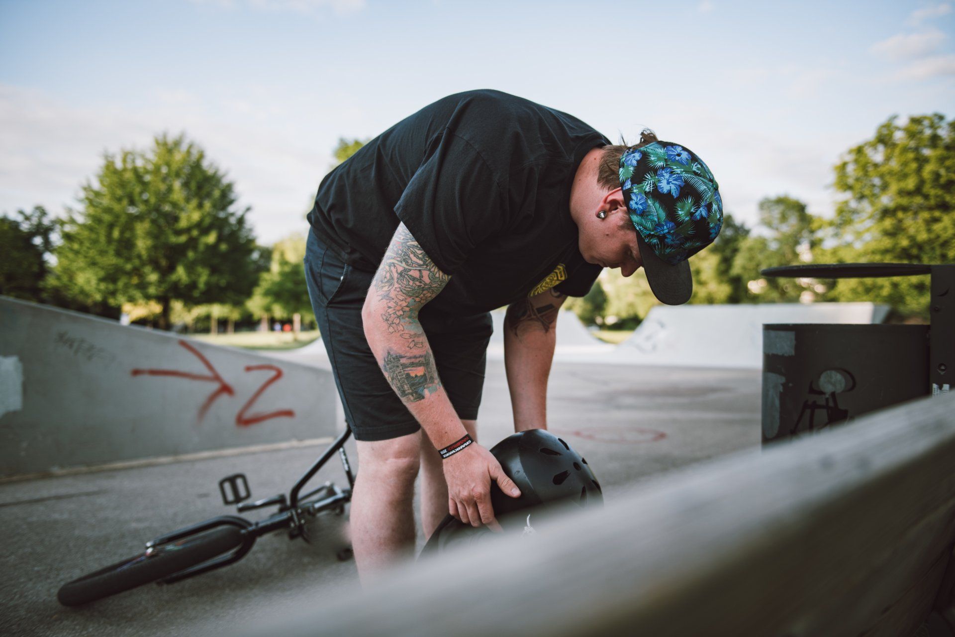 Mann in einem Skatepark bückt sich, um neben seinem umgestürzten BMX-Rad einen Helm aufzusetzen.