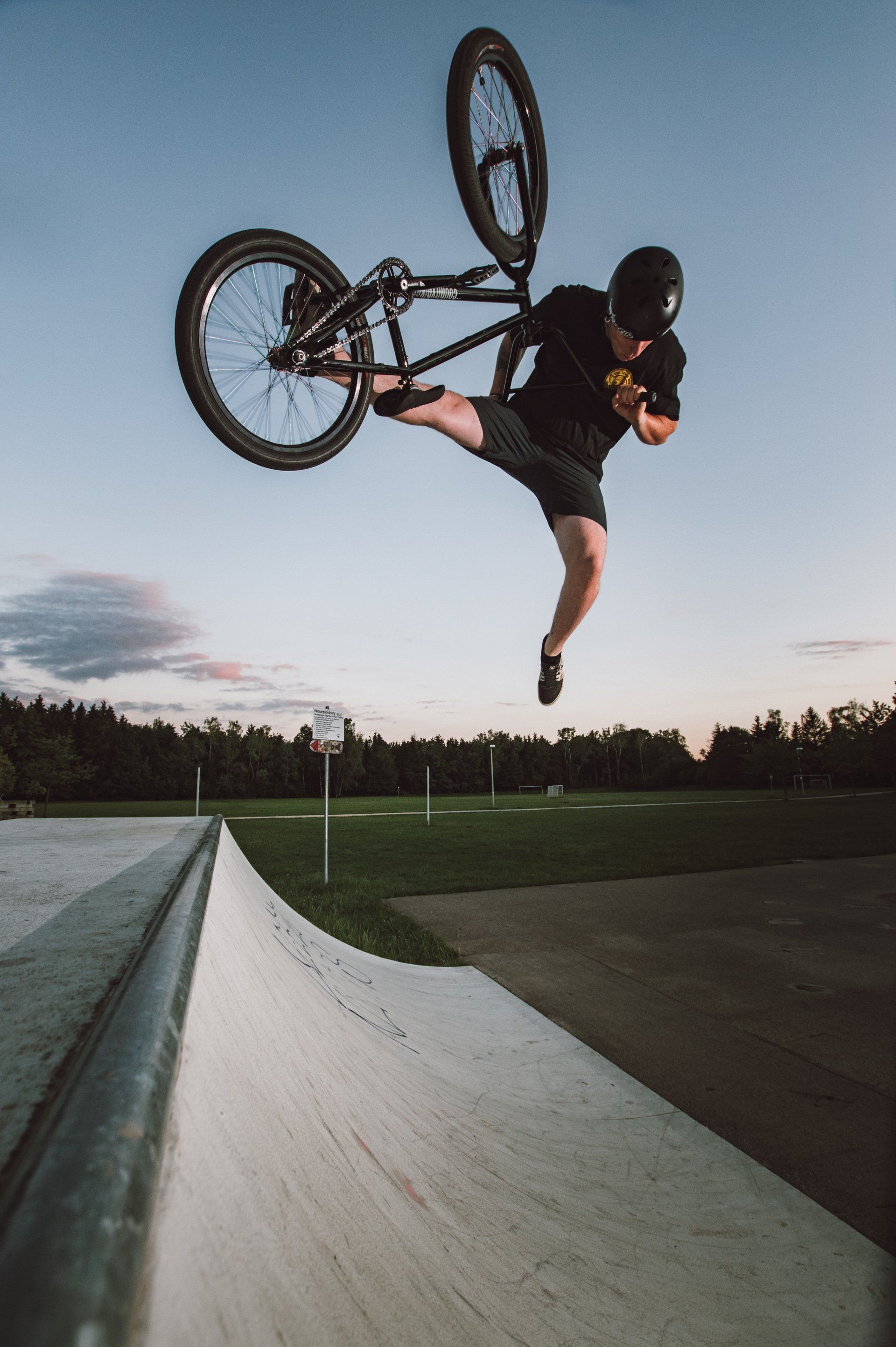 BMX-Fahrer führt in einem Skatepark einen Trick in der Luft aus. Der Fahrer ist schwarz und trägt schwarze Kleidung.