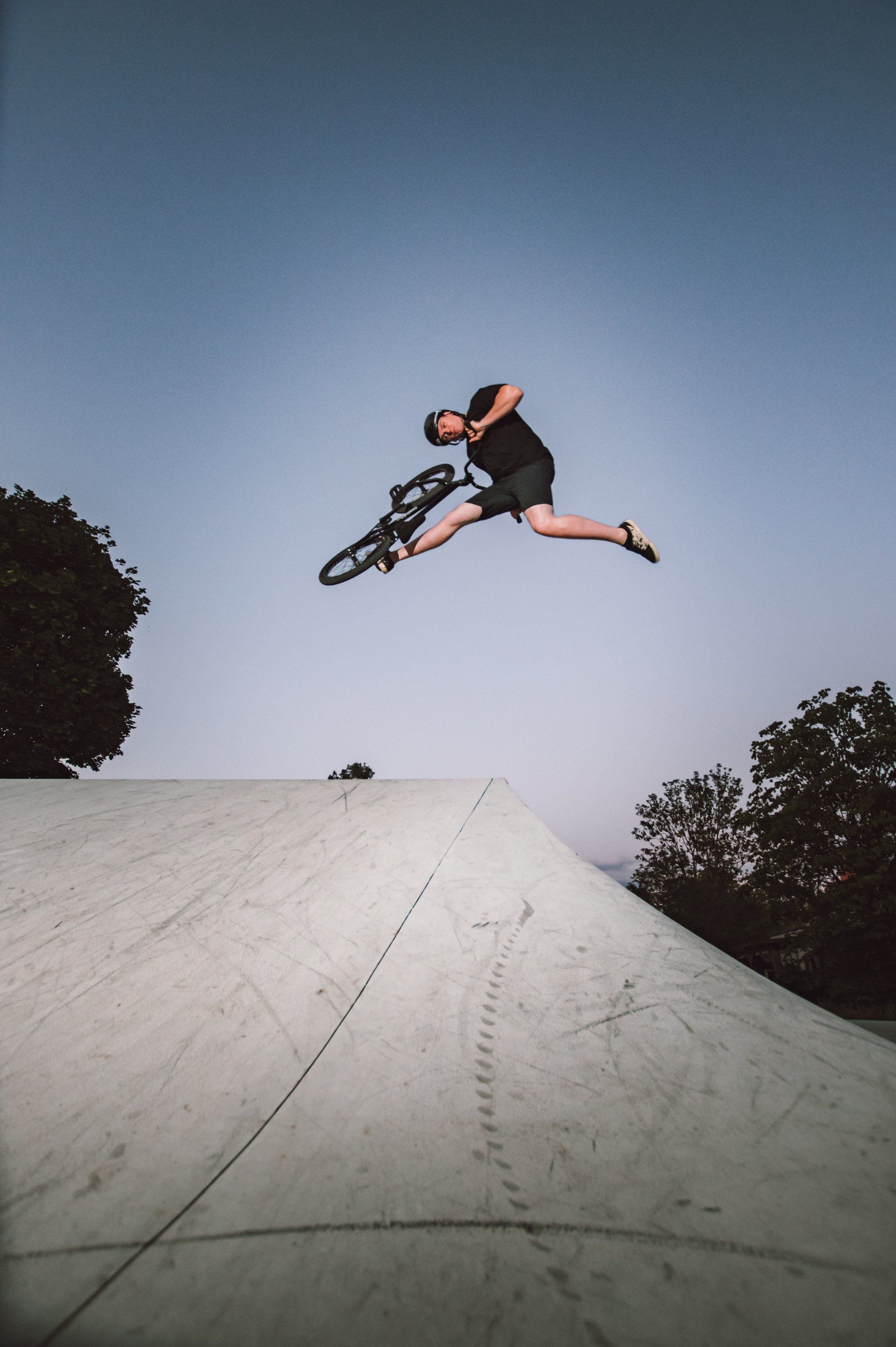 Mann auf Fahrrad springt vor blauem Himmel über eine Rampe in die Luft.