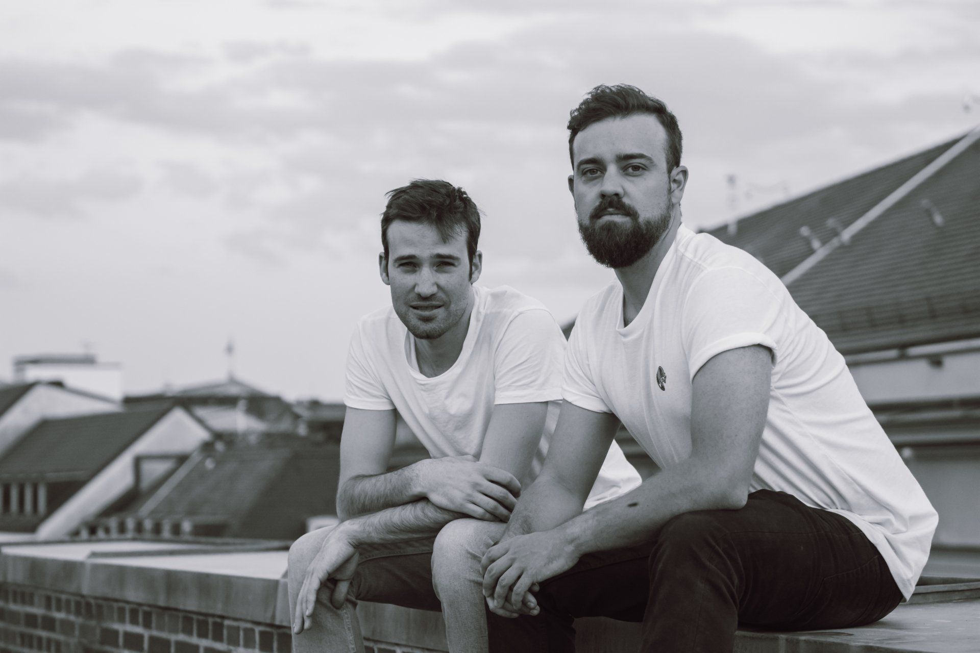 Zwei Männer in weißen Hemden und dunklen Hosen sitzen auf einem Dach. Schwarzweißfoto.