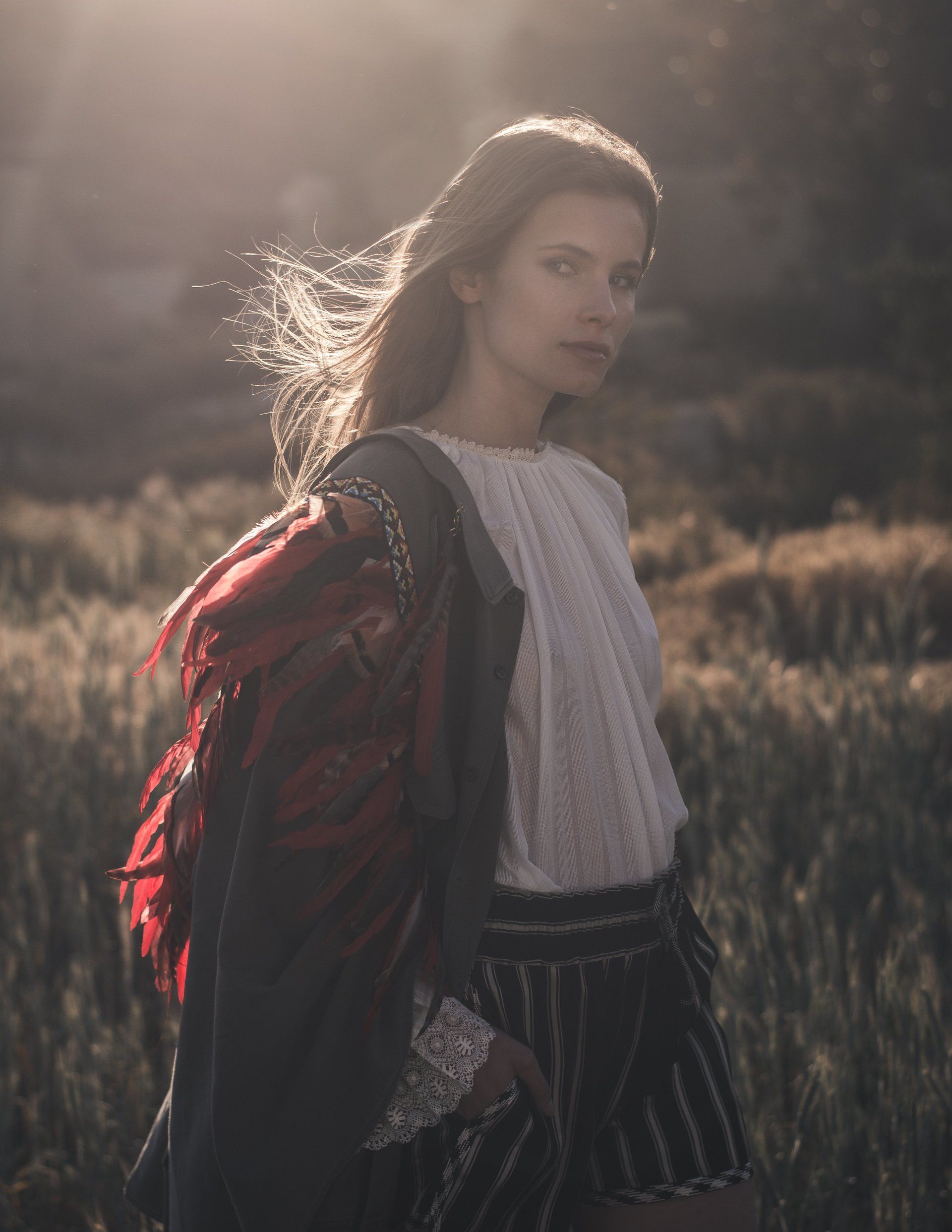 Frau in weißem Oberteil und Schal steht auf einem Feld und blickt in die Kamera.