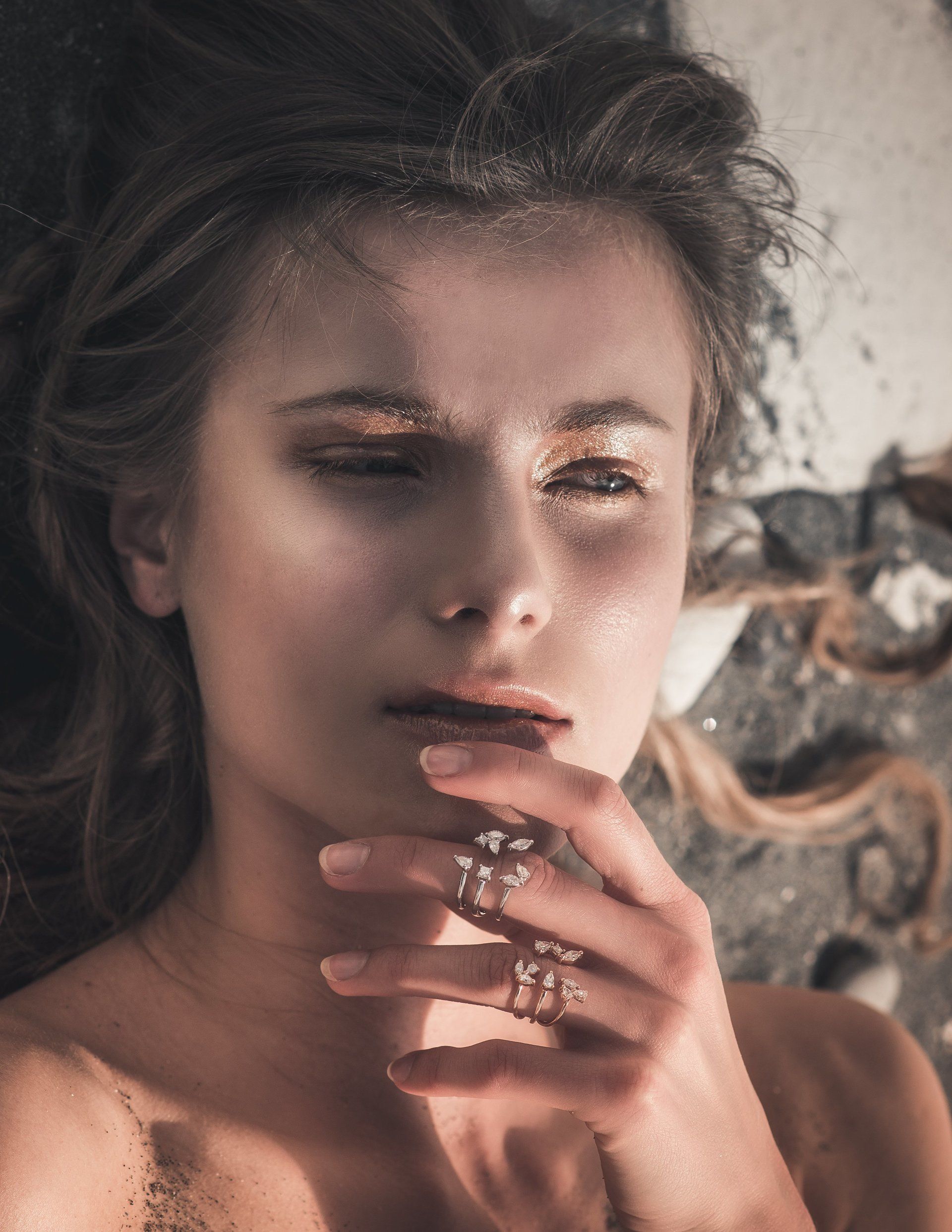 Frau mit goldenem Lidschatten, Hand in der Nähe des Gesichts, auf einer Oberfläche liegend.