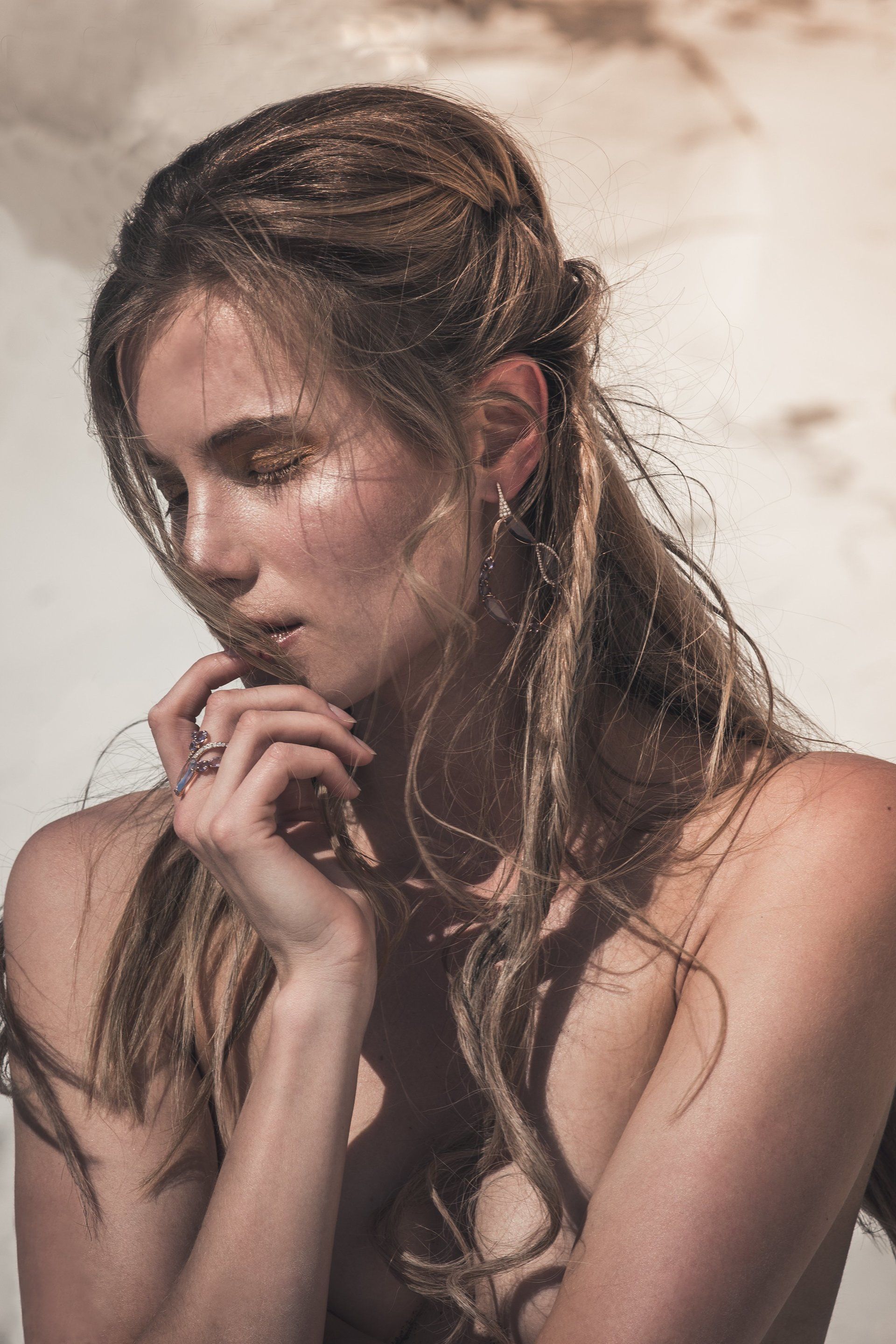 Frau mit welligem Haar und Glitzer-Make-up, blickt nach unten, Hand am Kinn.