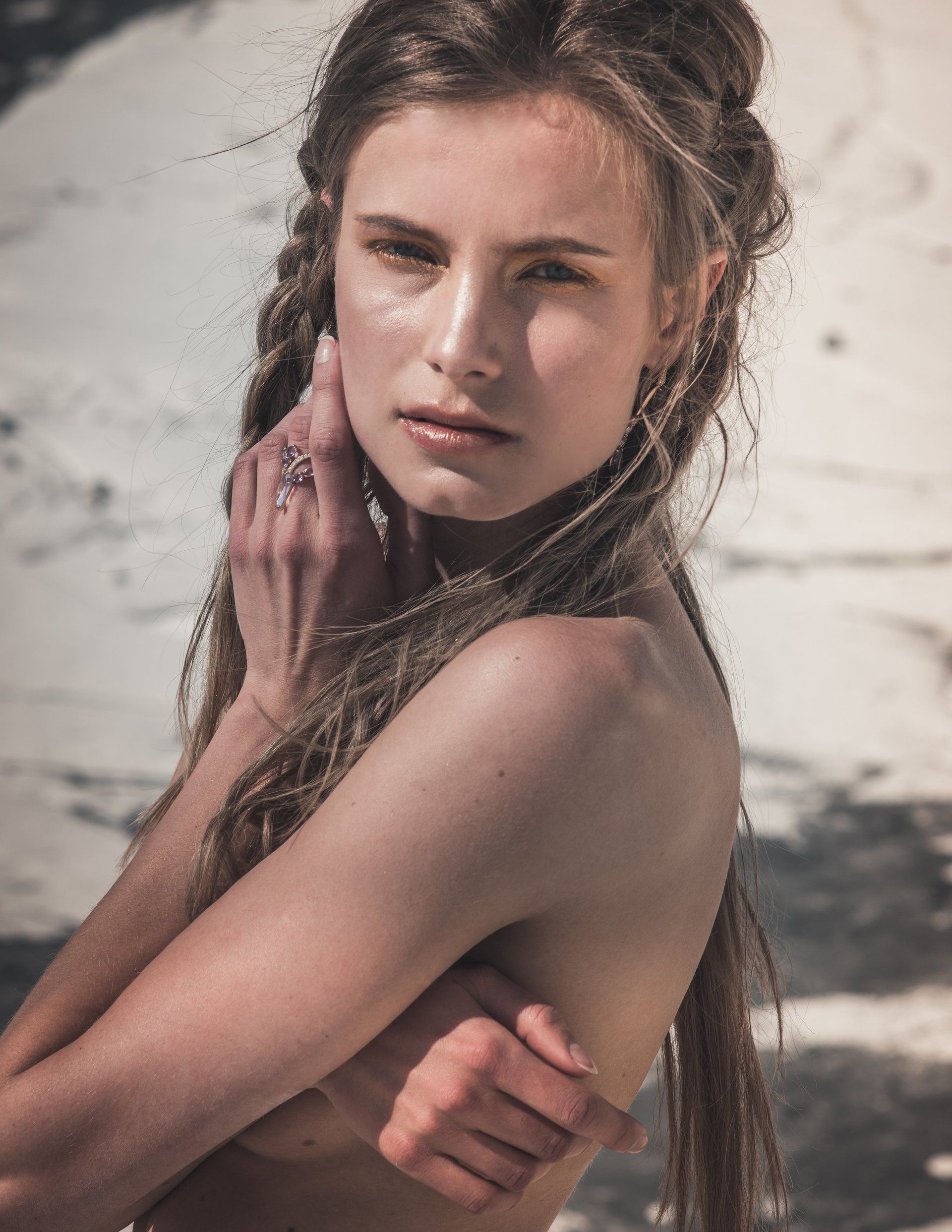 Frau mit langen Haaren, in natürlicher Umgebung, bedeckt ihre Brust und blickt den Betrachter an.