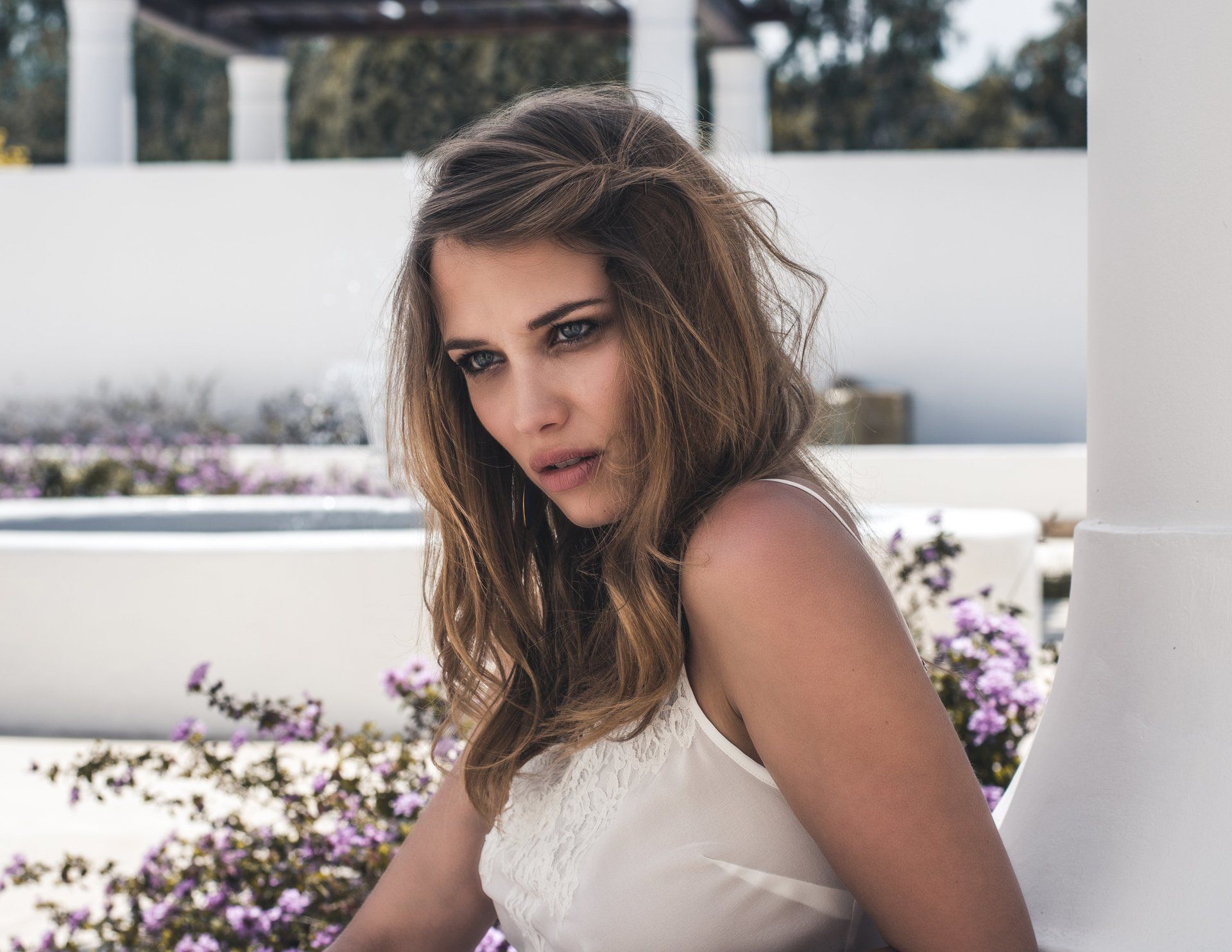 Frau mit hellbraunem Haar, trägt ein weißes Oberteil, blickt nach unten und sitzt im Freien.