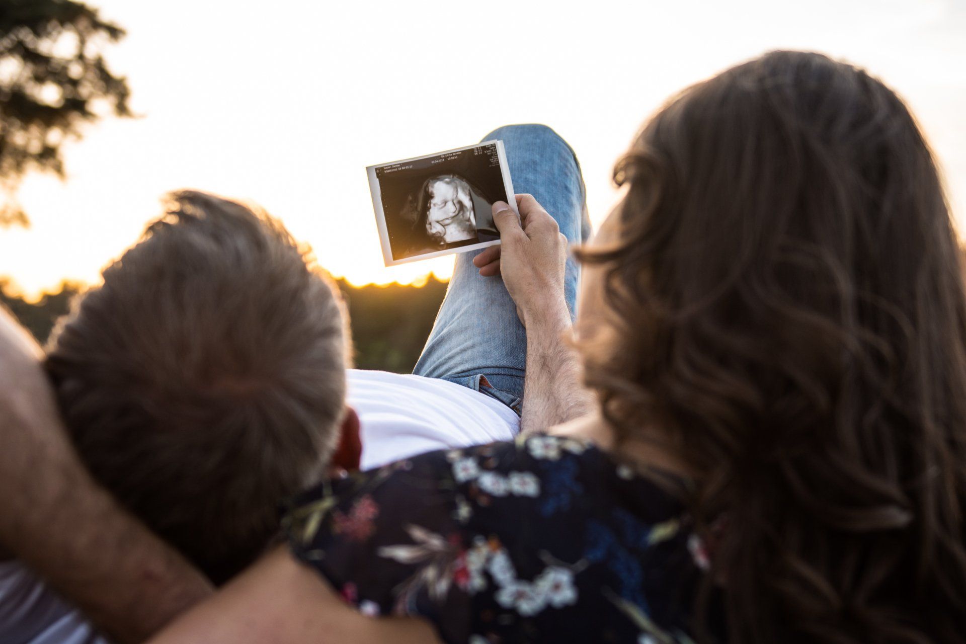 Paar im Freien, betrachtet Ultraschallbild, Gegenlicht durch Sonnenuntergang.