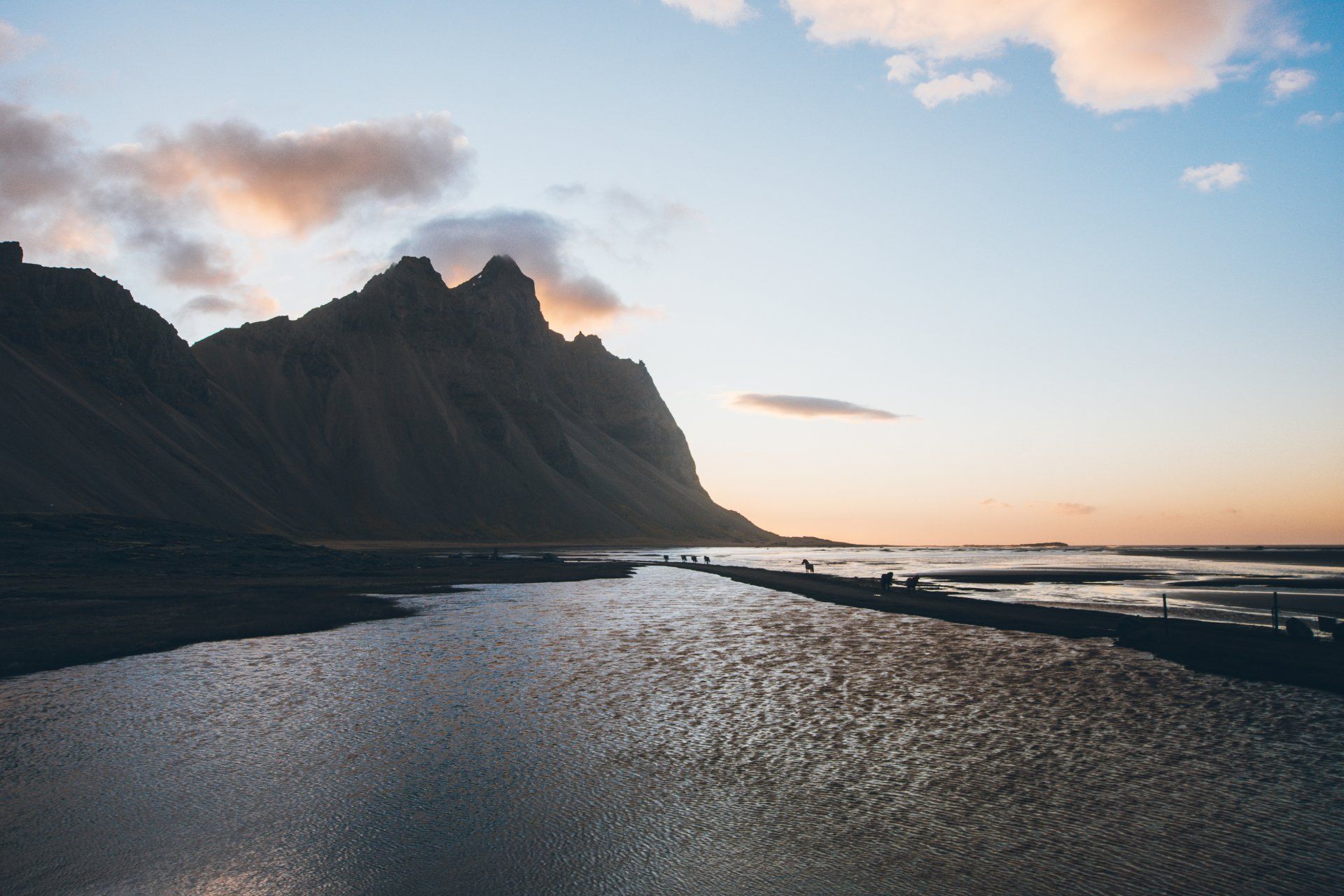 Berge und Wasser in der Abenddämmerung, mit Menschen, die im Vordergrund auf einem Bauwerk laufen.