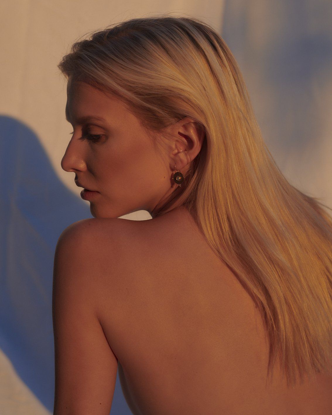 Blonde Frau mit langen Haaren, Blick nach unten. Warmes Licht, nackte Schultern.