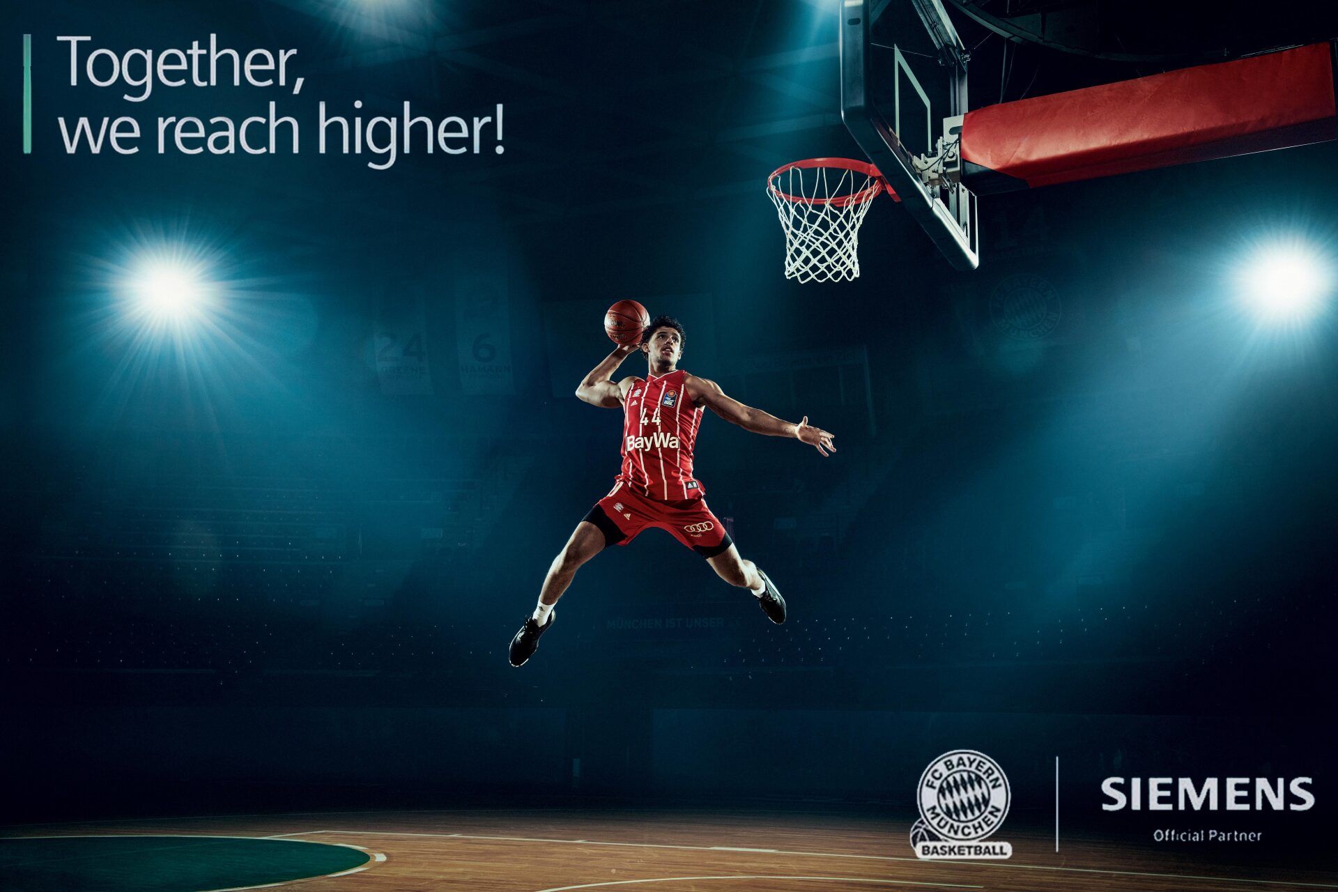 Basketballspieler springt zum Dunk, dramatisch beleuchtet in einer dunklen Arena. 