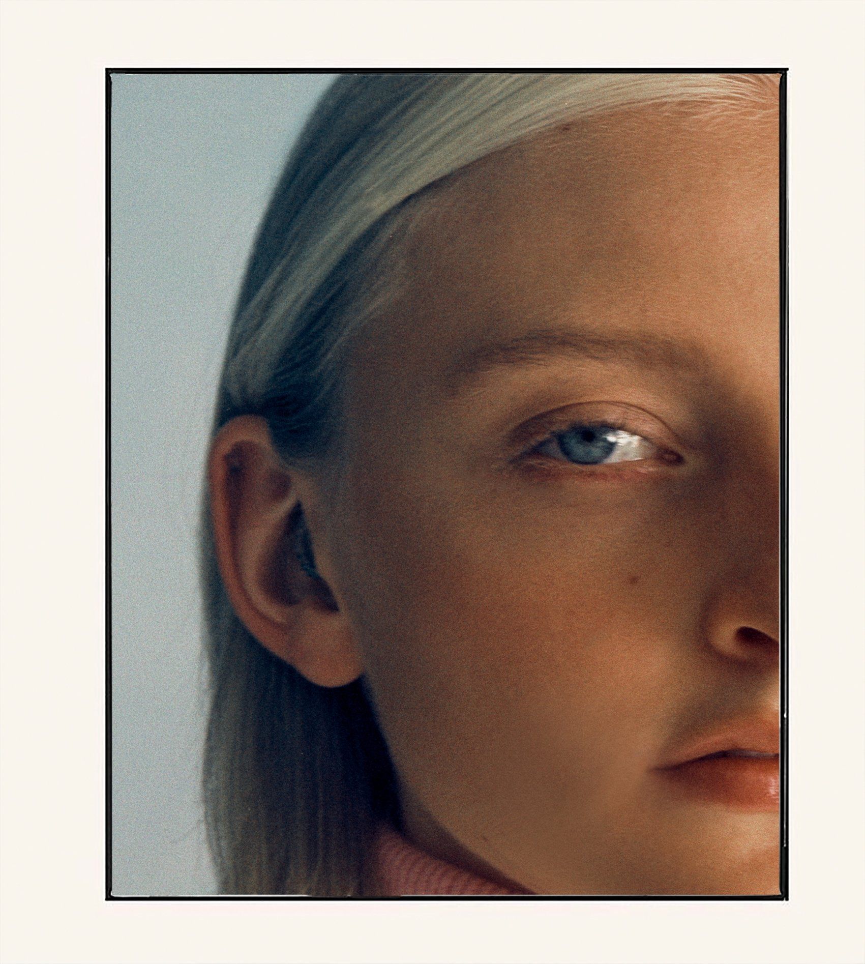 Nahaufnahme des Gesichts einer Frau, helle Haut, blaue Augen, blondes Haar, rosa Rollkragenpullover.