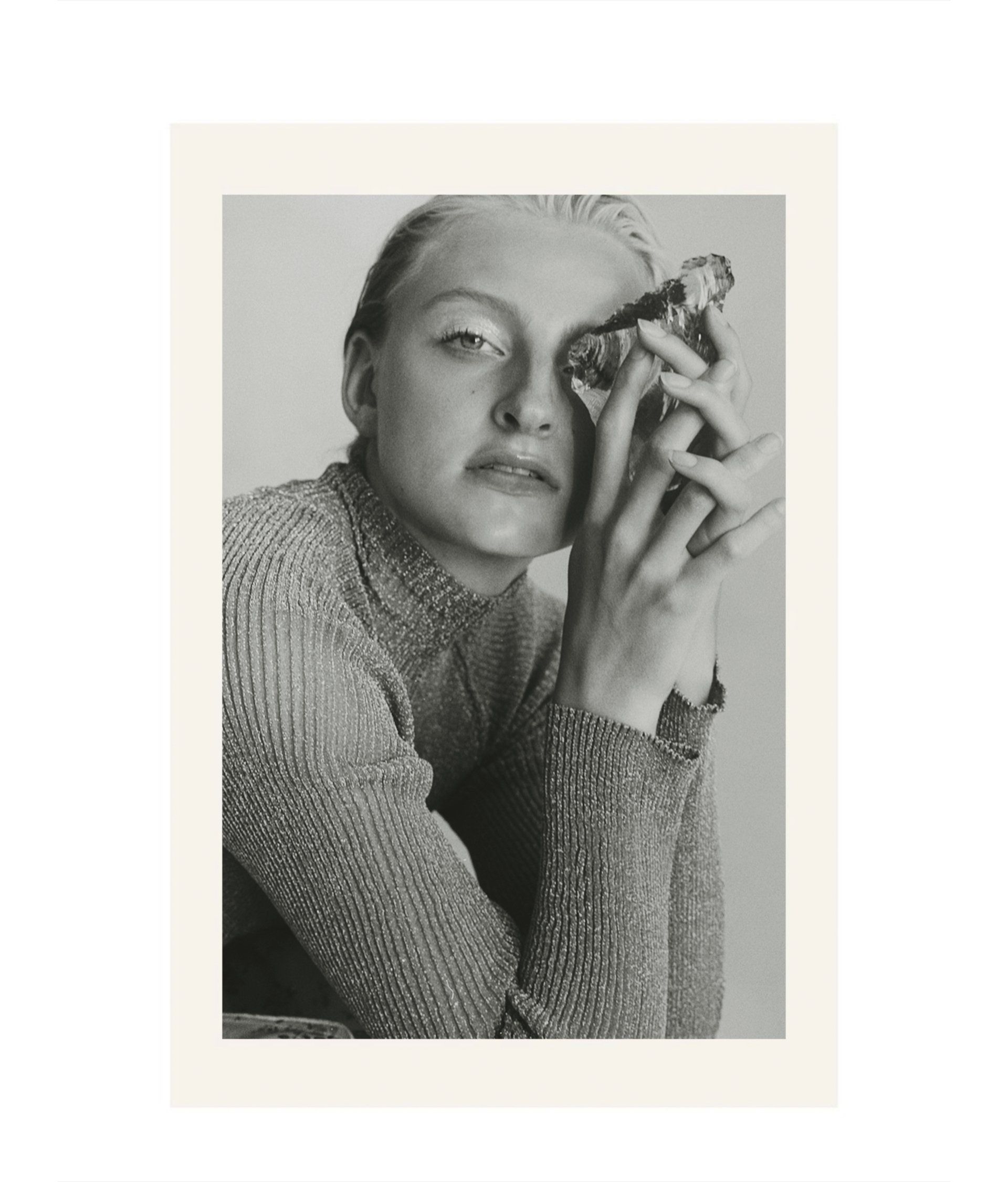 Frau im glitzernden Rollkragenpullover hält einen kleinen Gegenstand vor ihr Auge; Schwarzweißporträt.