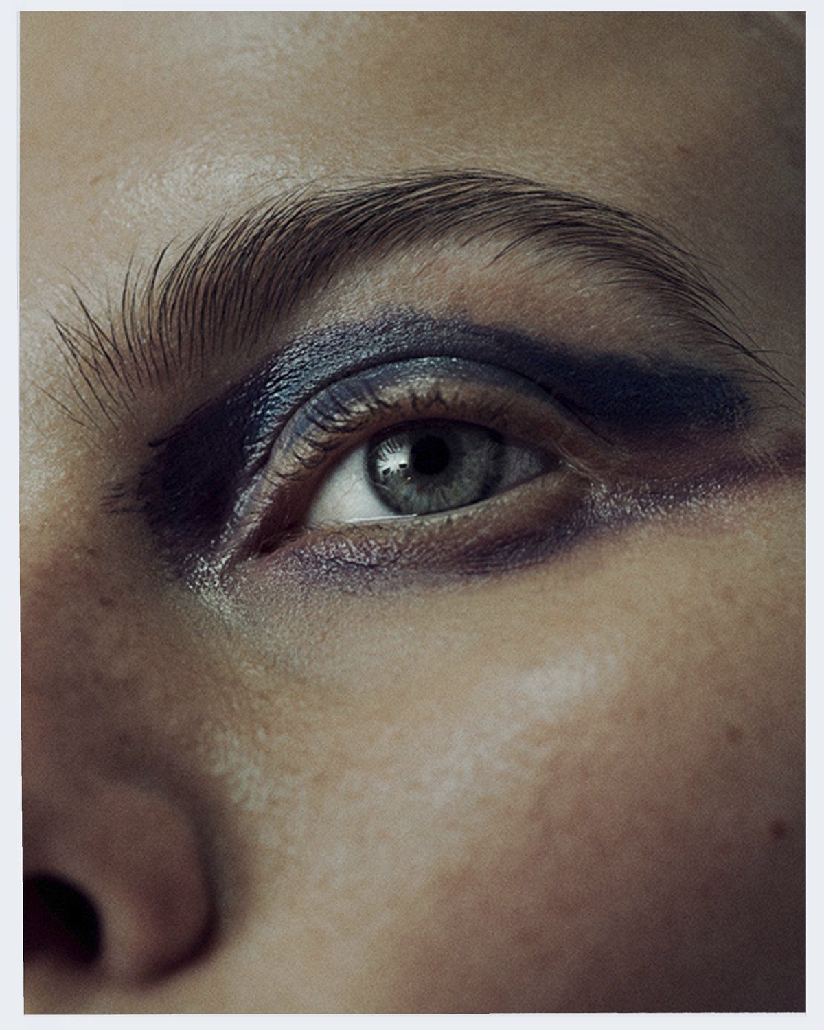 Nahaufnahme eines Auges mit dunkelblauem Lidschatten und grauer Iris.