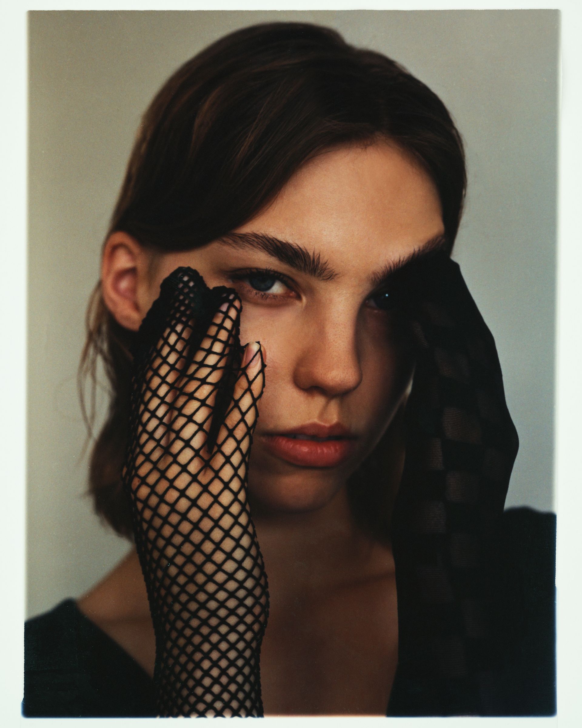 Frau mit dunklem Haar, die schwarze Netzhandschuhe trägt und den Betrachter direkt ansieht.