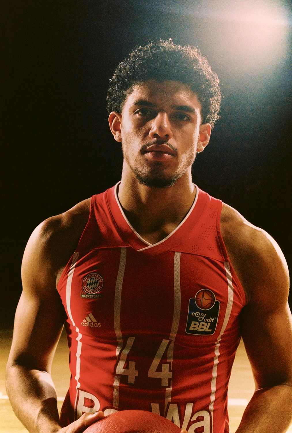 Basketballspieler im roten Trikot hält Ball, drinnen.