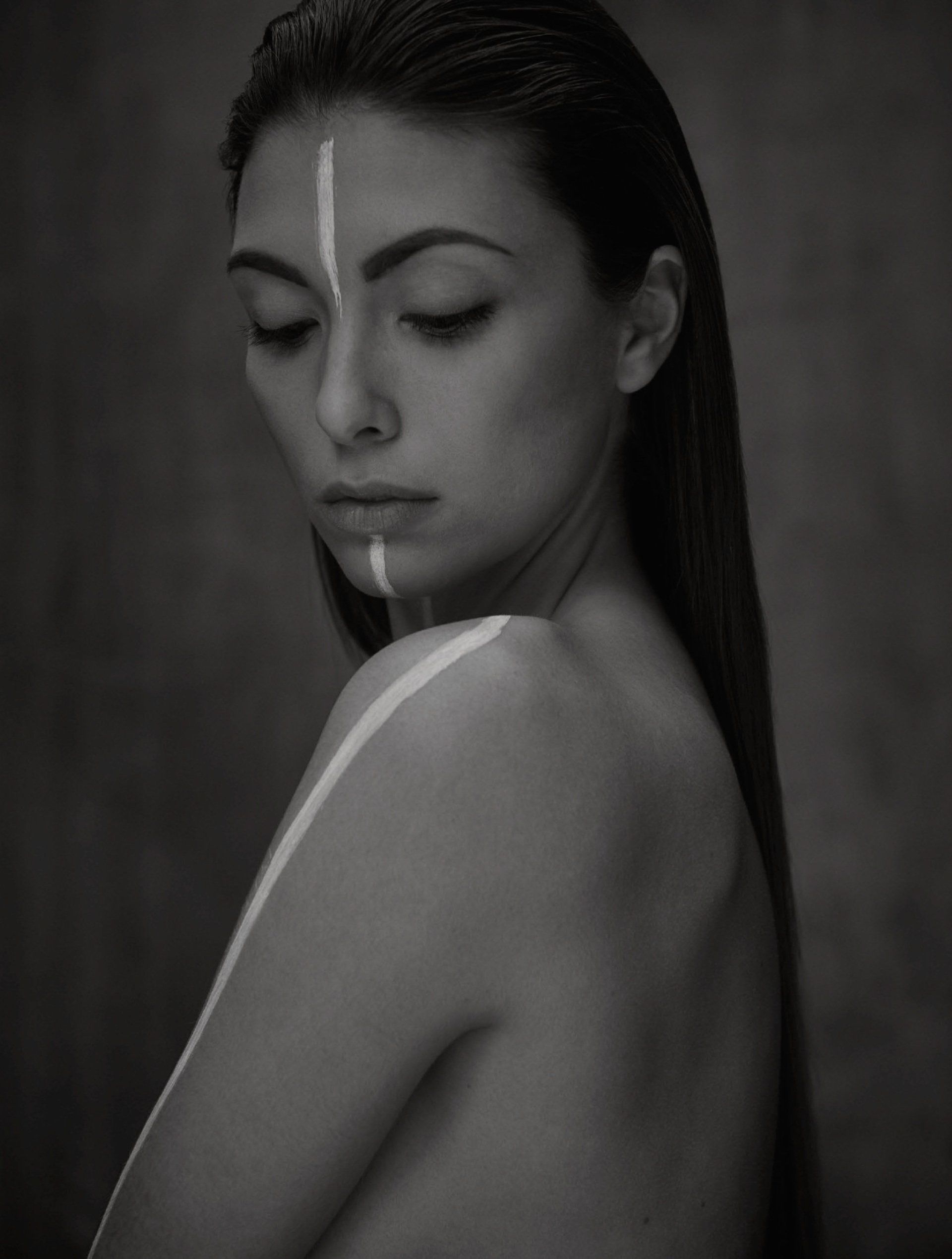 Frau mit dunklem Haar, weißer Gesichts-/Körperbemalung, Blick nach unten, Graustufen.