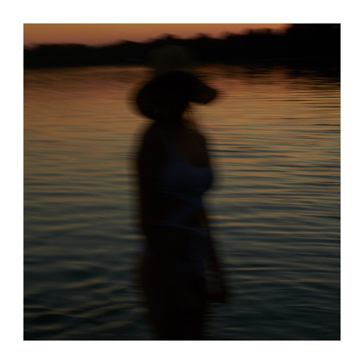 Silhouette einer Person im Wasser bei Sonnenuntergang, die einen Hut trägt.