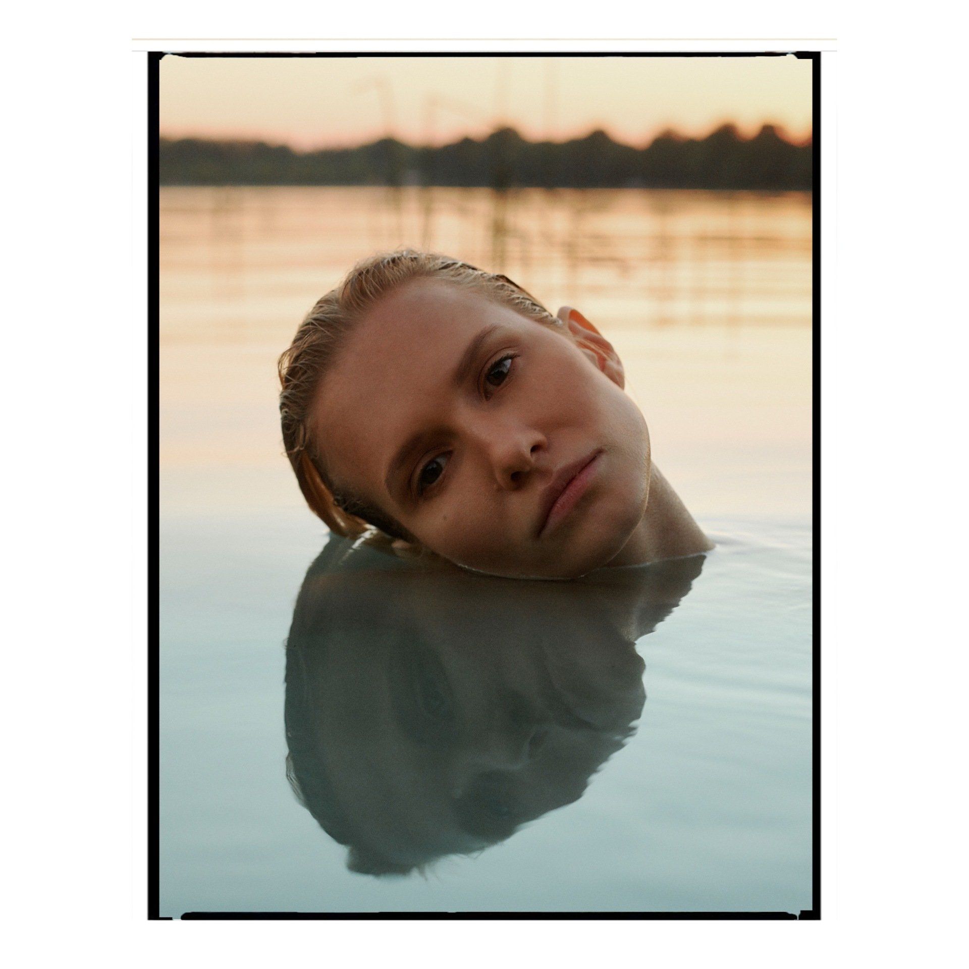 Kopf und Schultern einer Frau tauchen aus dem Wasser auf und blicken auf den Betrachter. 