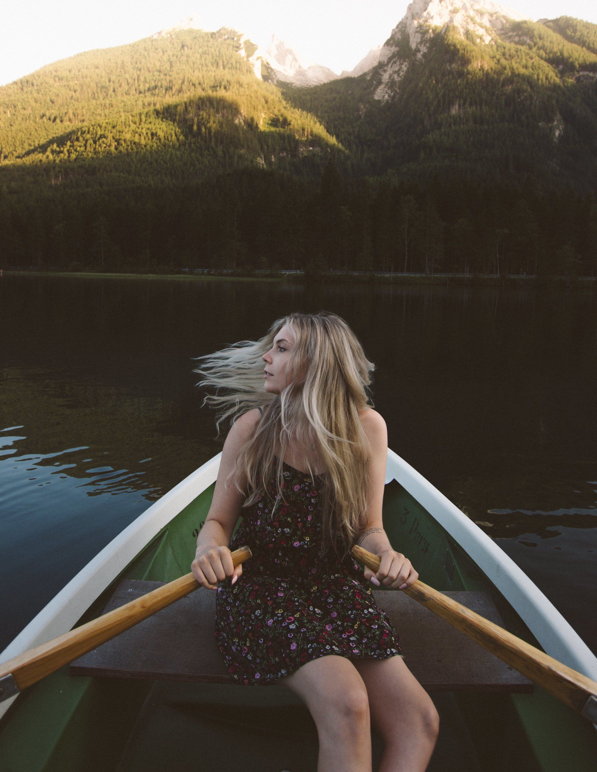 Frau rudert ein Boot auf einem See und blickt zurück auf die Berge.