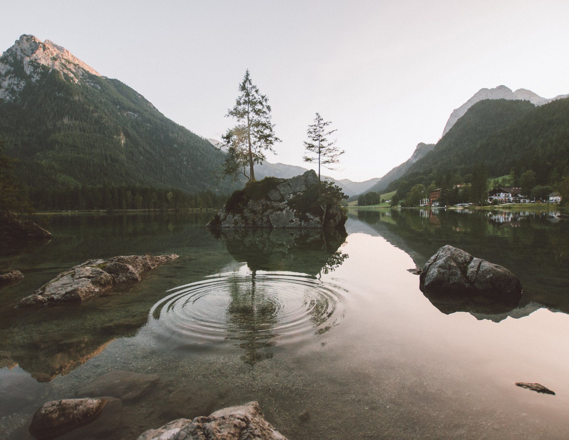 Seenlandschaft mit kleiner Insel, Bäumen und Bergen, die sich im Wasser spiegeln.