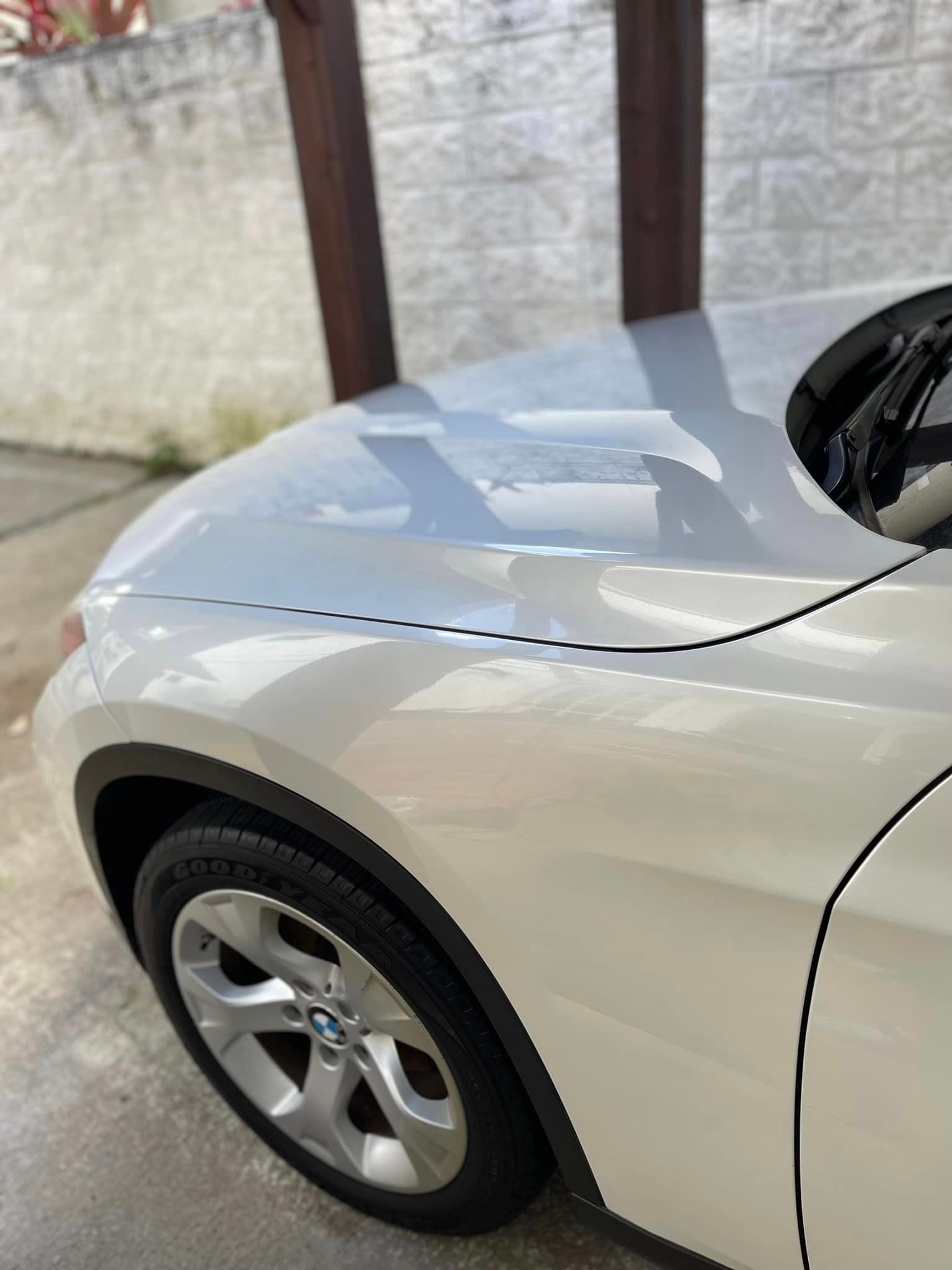 A white car is parked in a driveway next to a brick wall.