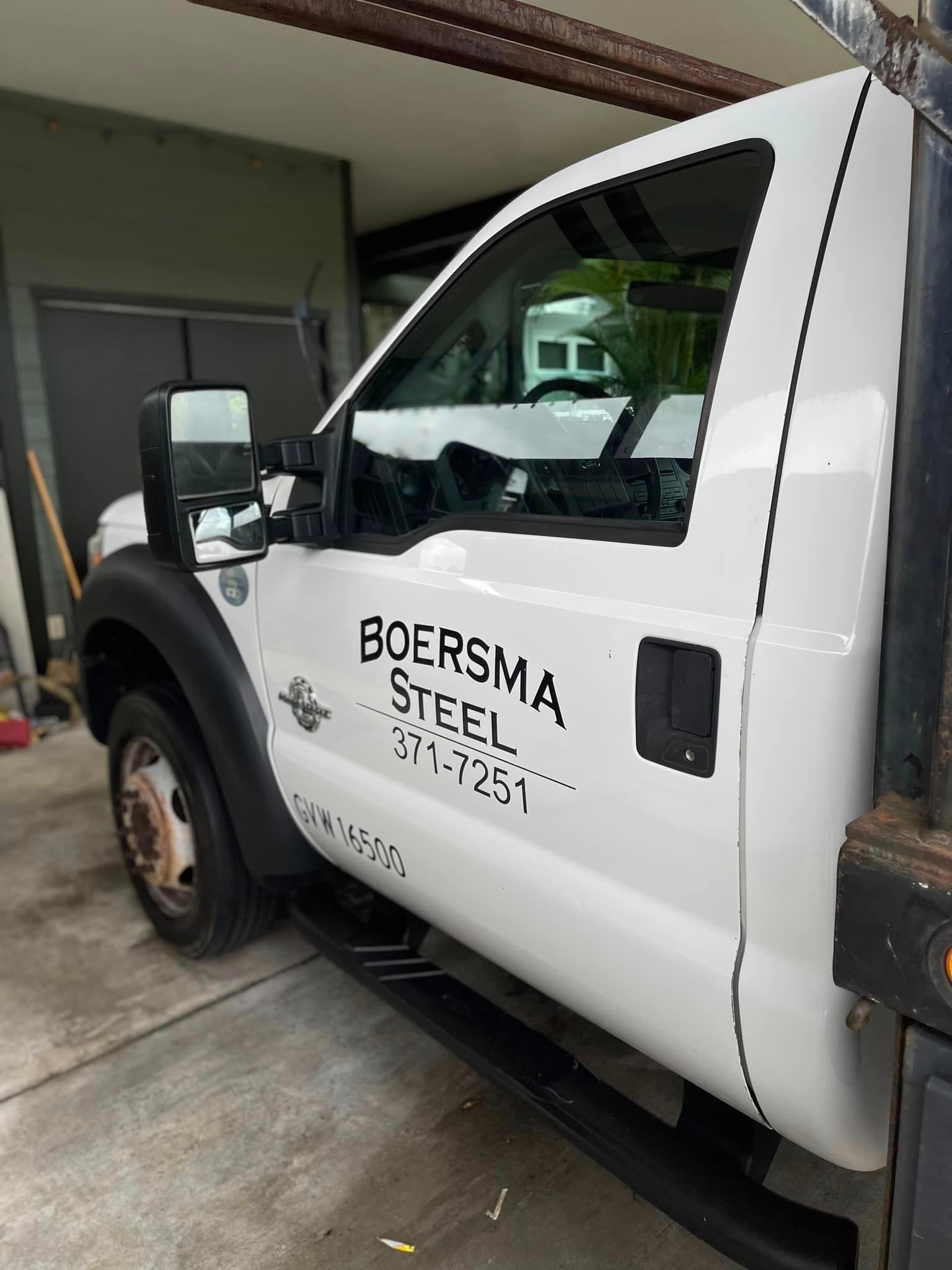 A white boersma steel truck is parked in front of a building.
