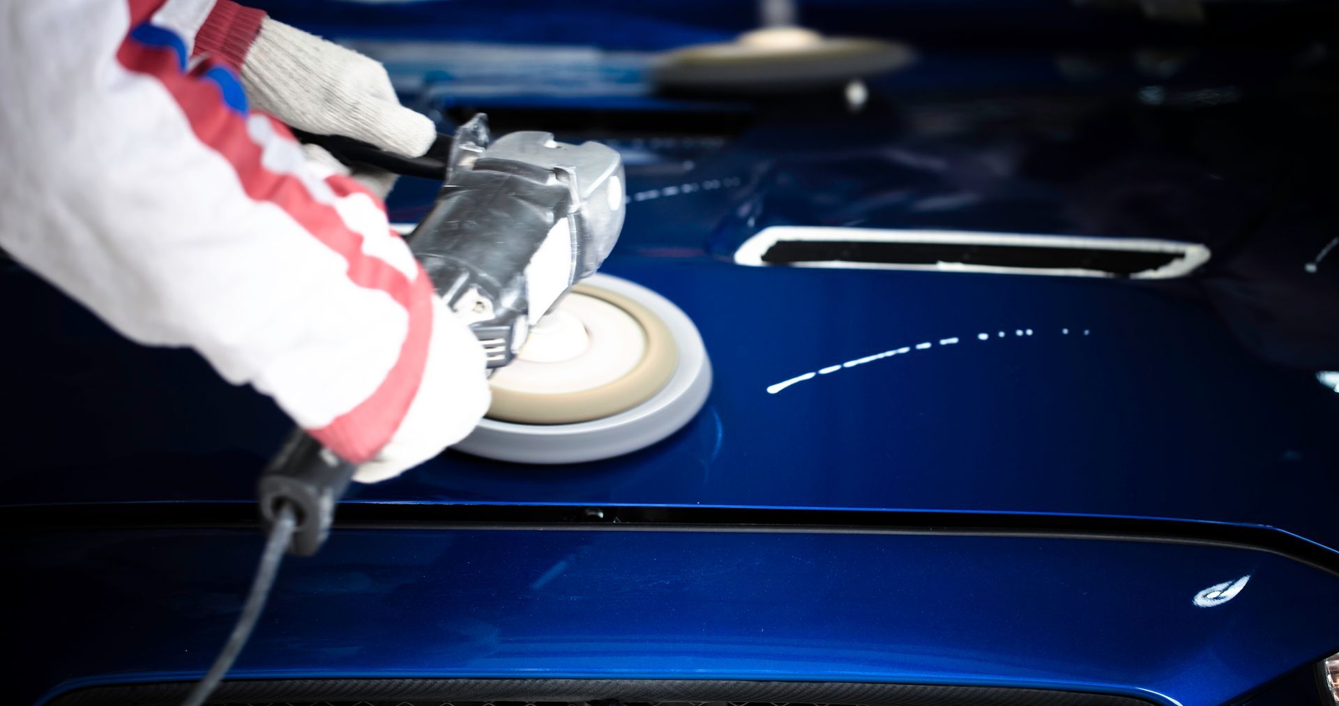 A person is polishing a blue car with a machine.